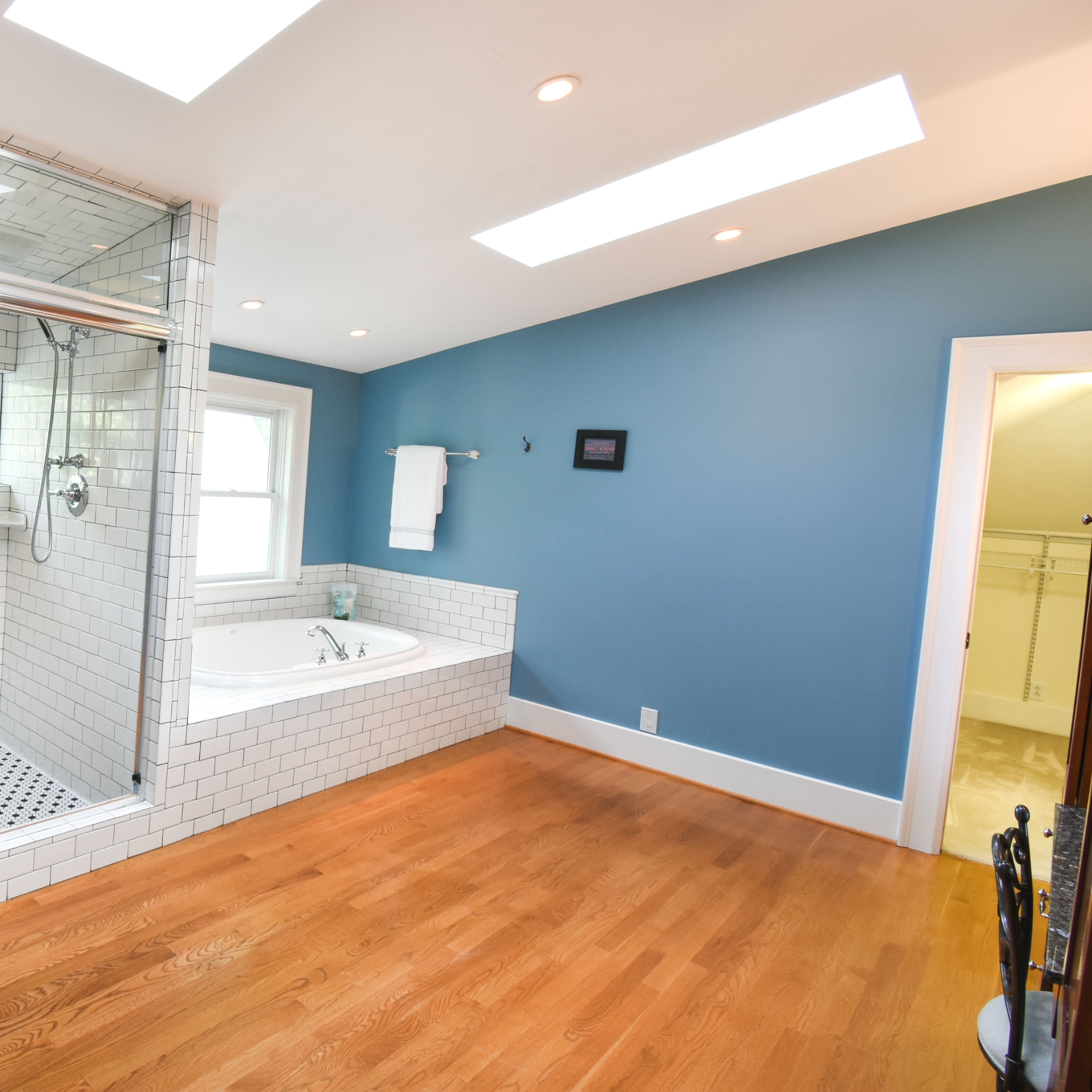 A modern bathroom featuring a glass-enclosed shower with white subway tiles and a freestanding bathtub beside it, all set against a blue wall.