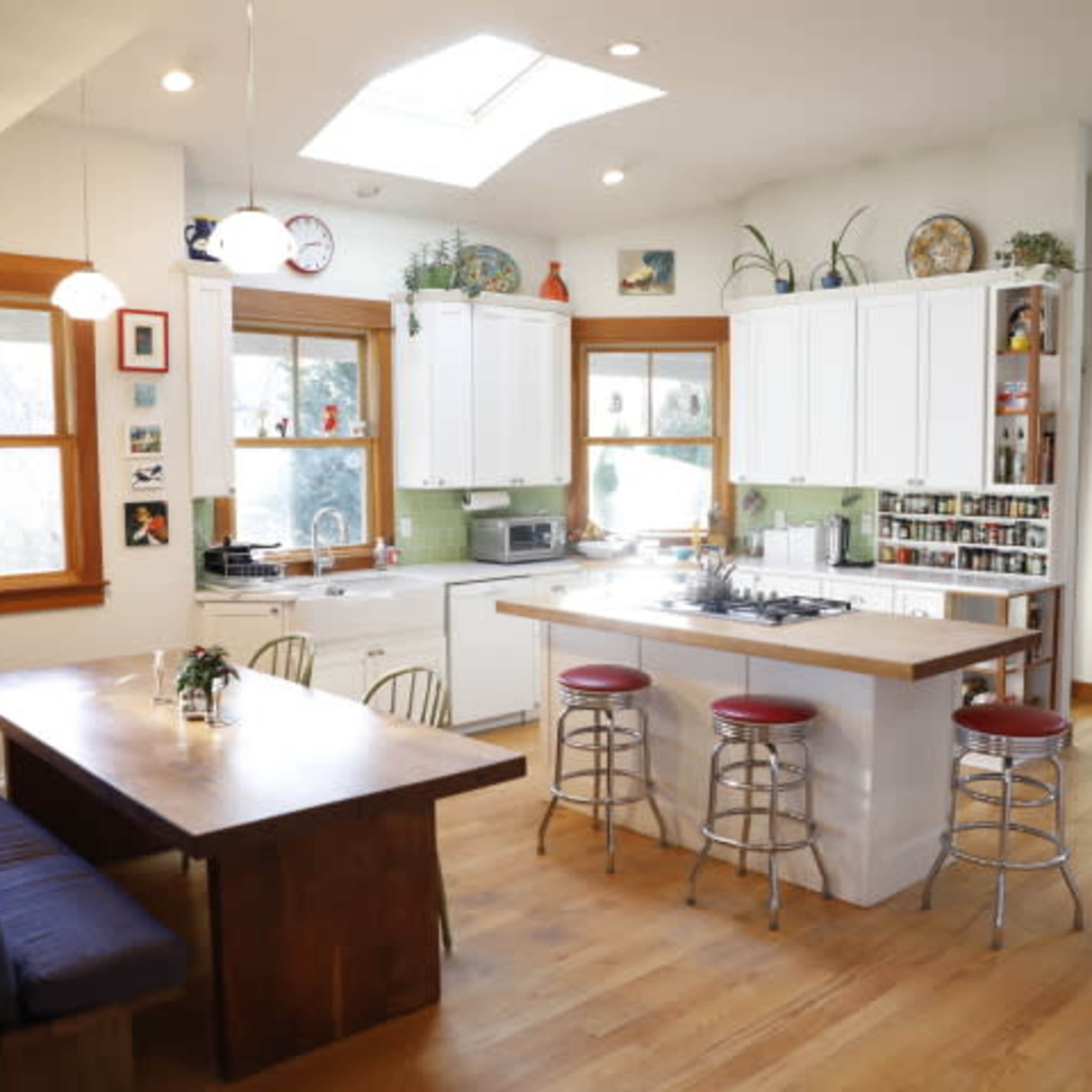 A bright, open kitchen with white cabinetry, a central island with bar seating, and a dining table adjacent to the windows.