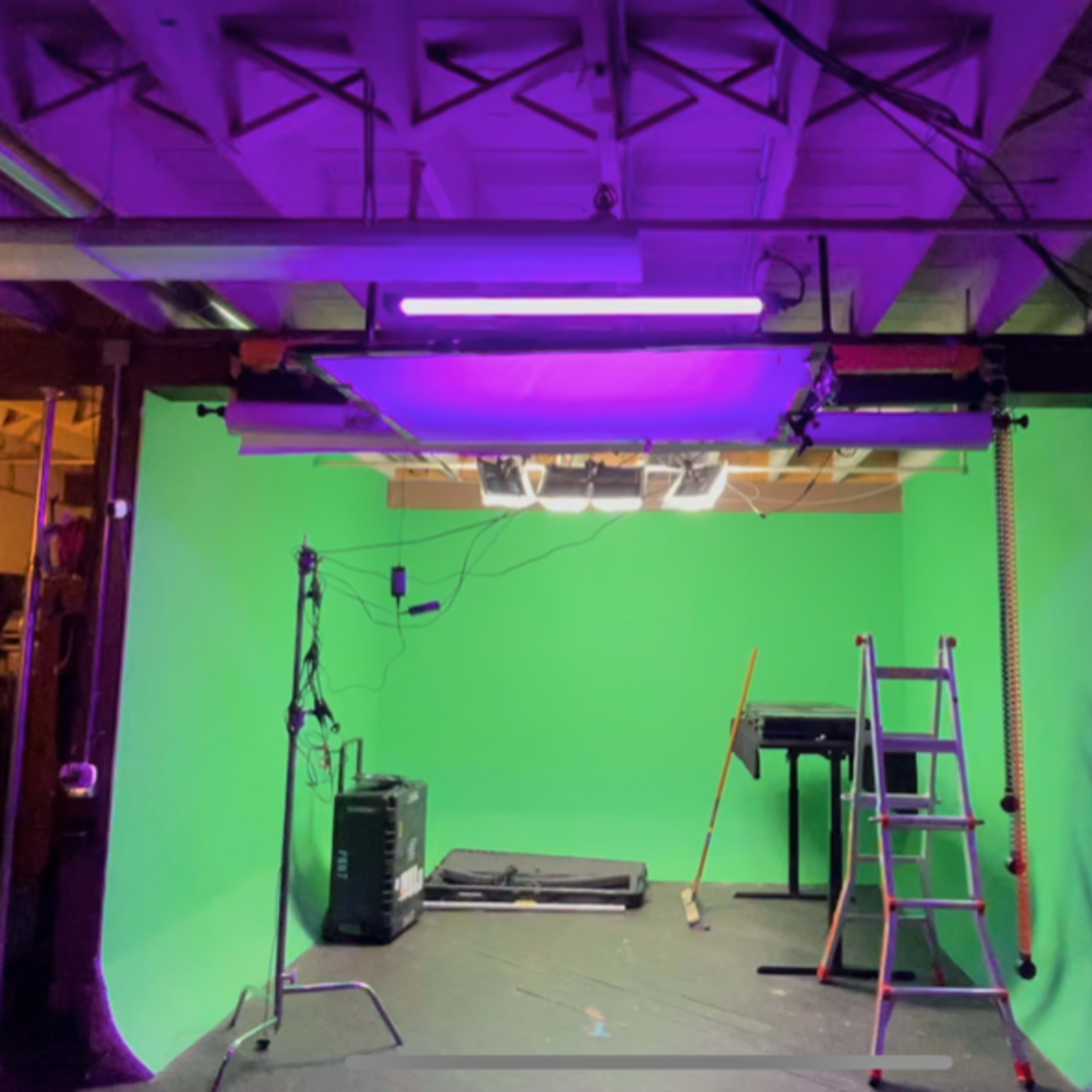 A studio setup with a green screen, lighting equipment, a ladder, and various props arranged in a spacious room.