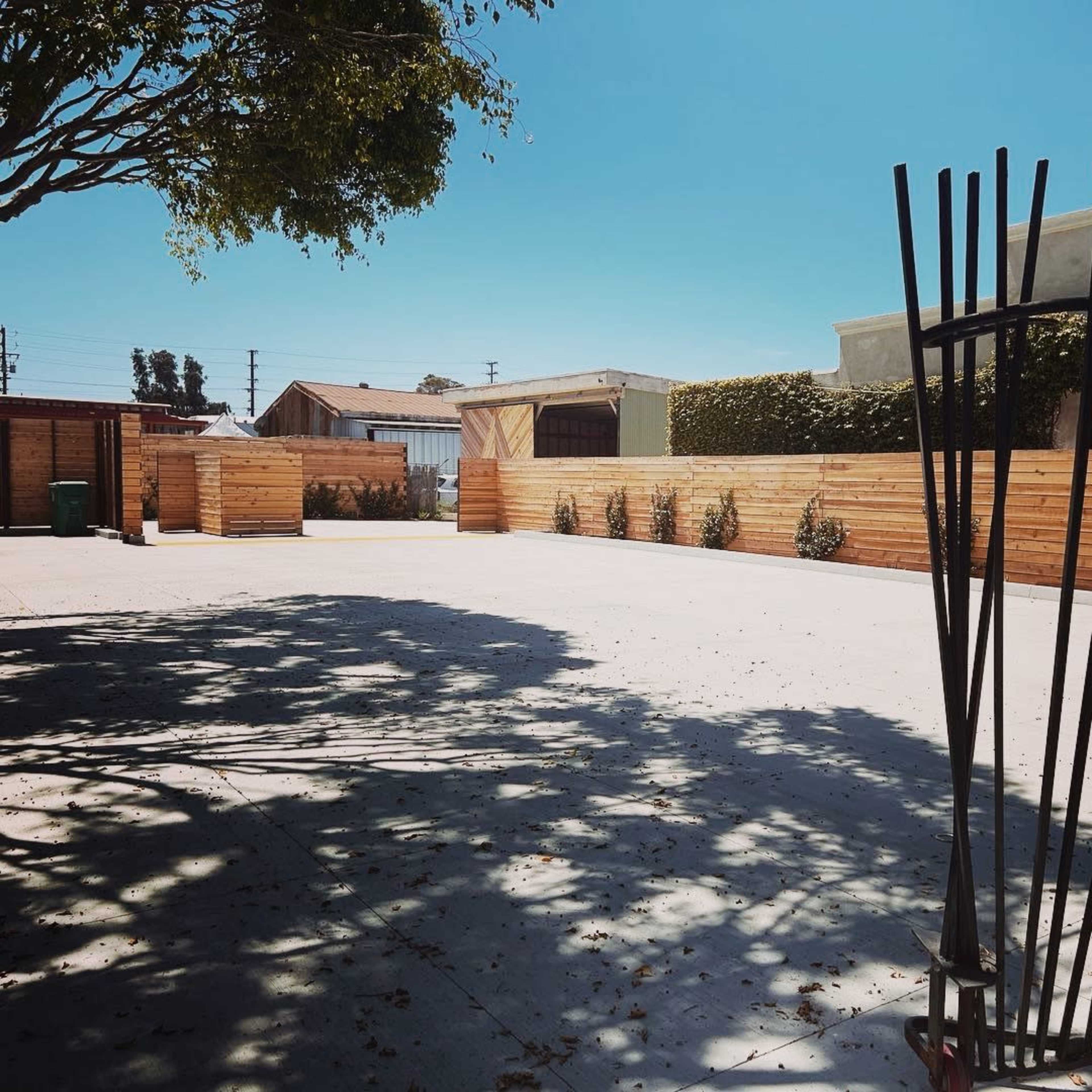 A cleared outdoor space with a metal gate and wooden fencing, surrounded by trees and buildings.