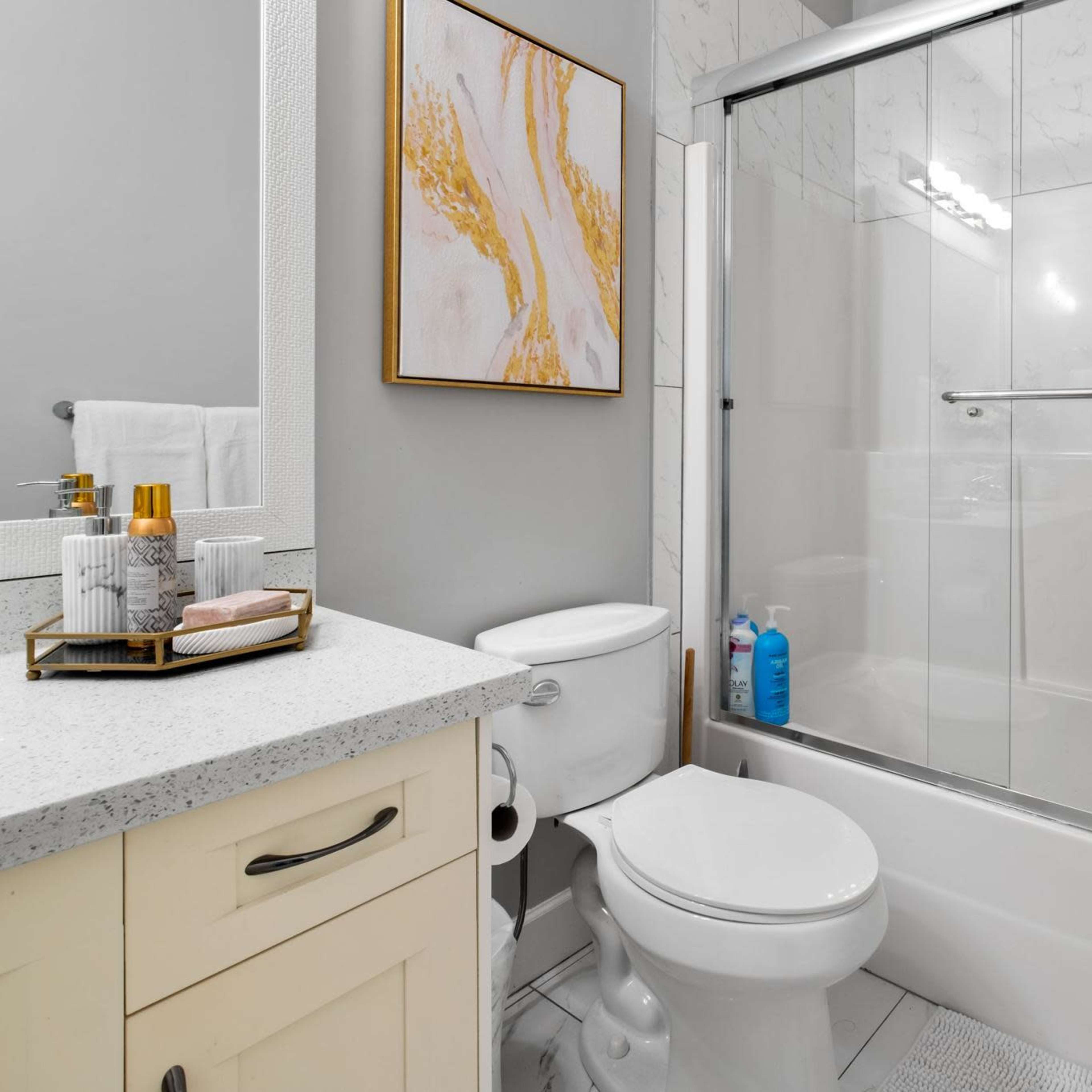 A modern bathroom with a shower/tub combination, a white vanity with a countertop, and decorative items on the counter.