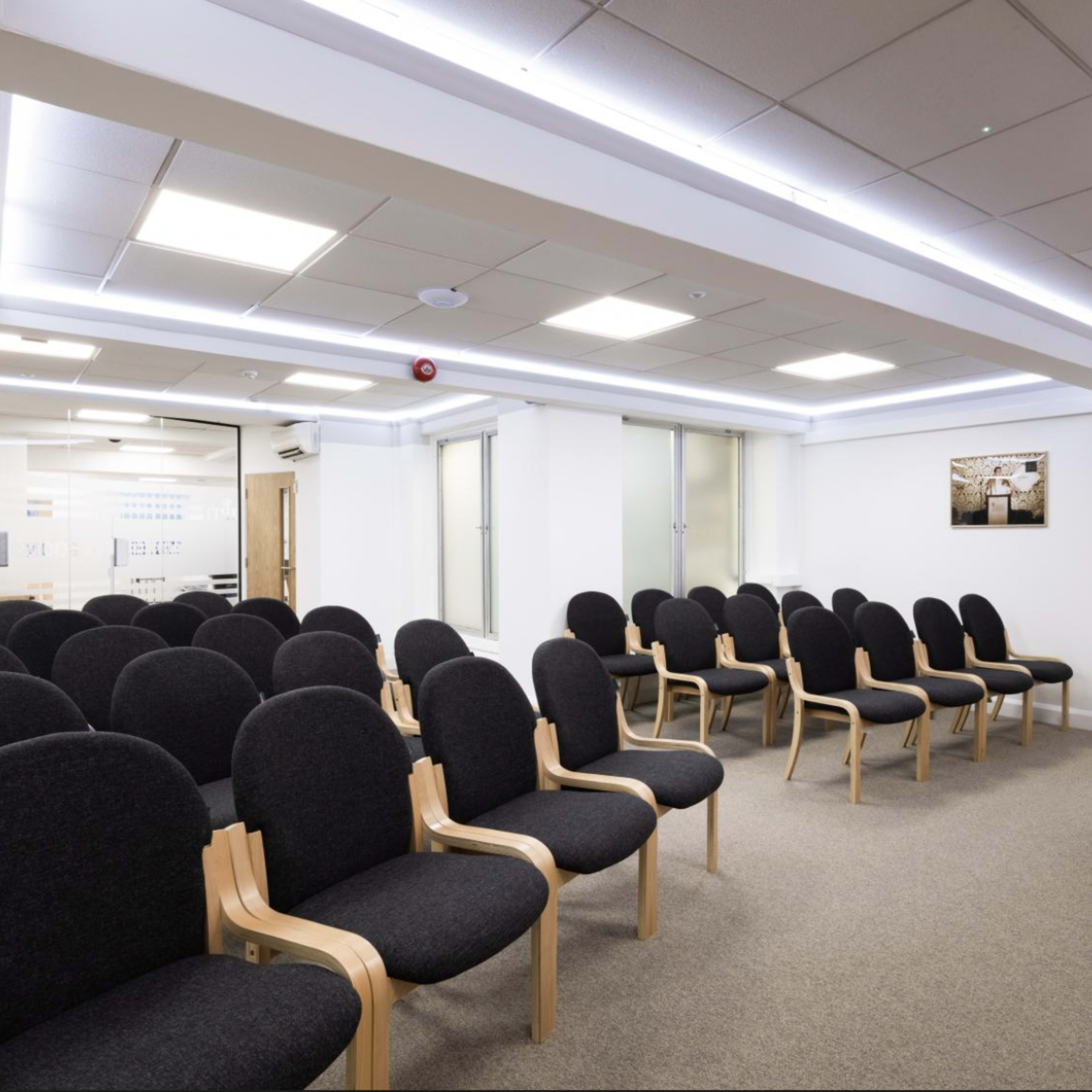 A modern conference room with rows of black upholstered chairs facing a wooden podium.