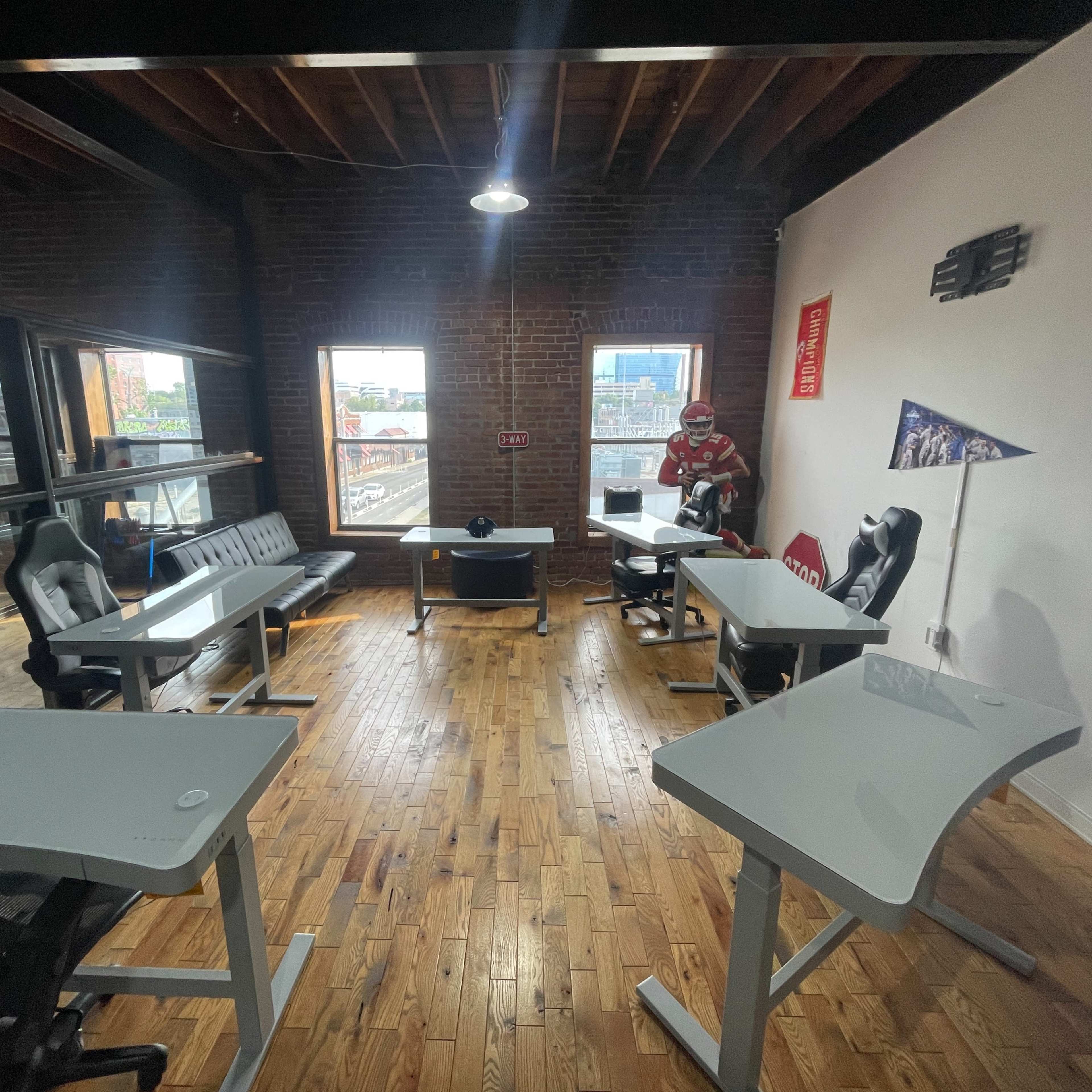 A modern office space features several desks arranged in two clusters, with large windows providing natural light and a view of the city.