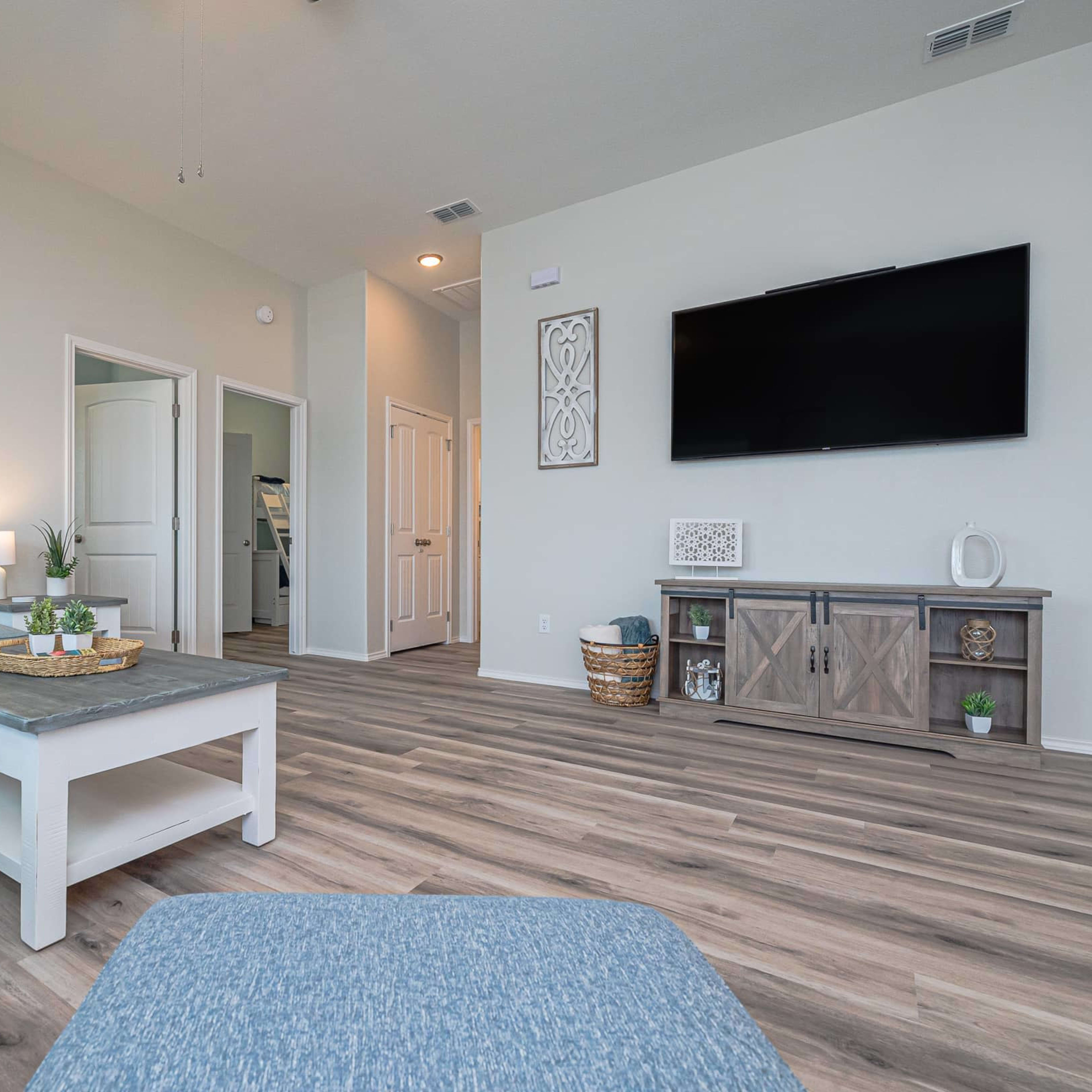 A modern living room with a light gray sectional sofa, a wooden coffee table, and a wall-mounted television, all set against a neutral-colored wall.