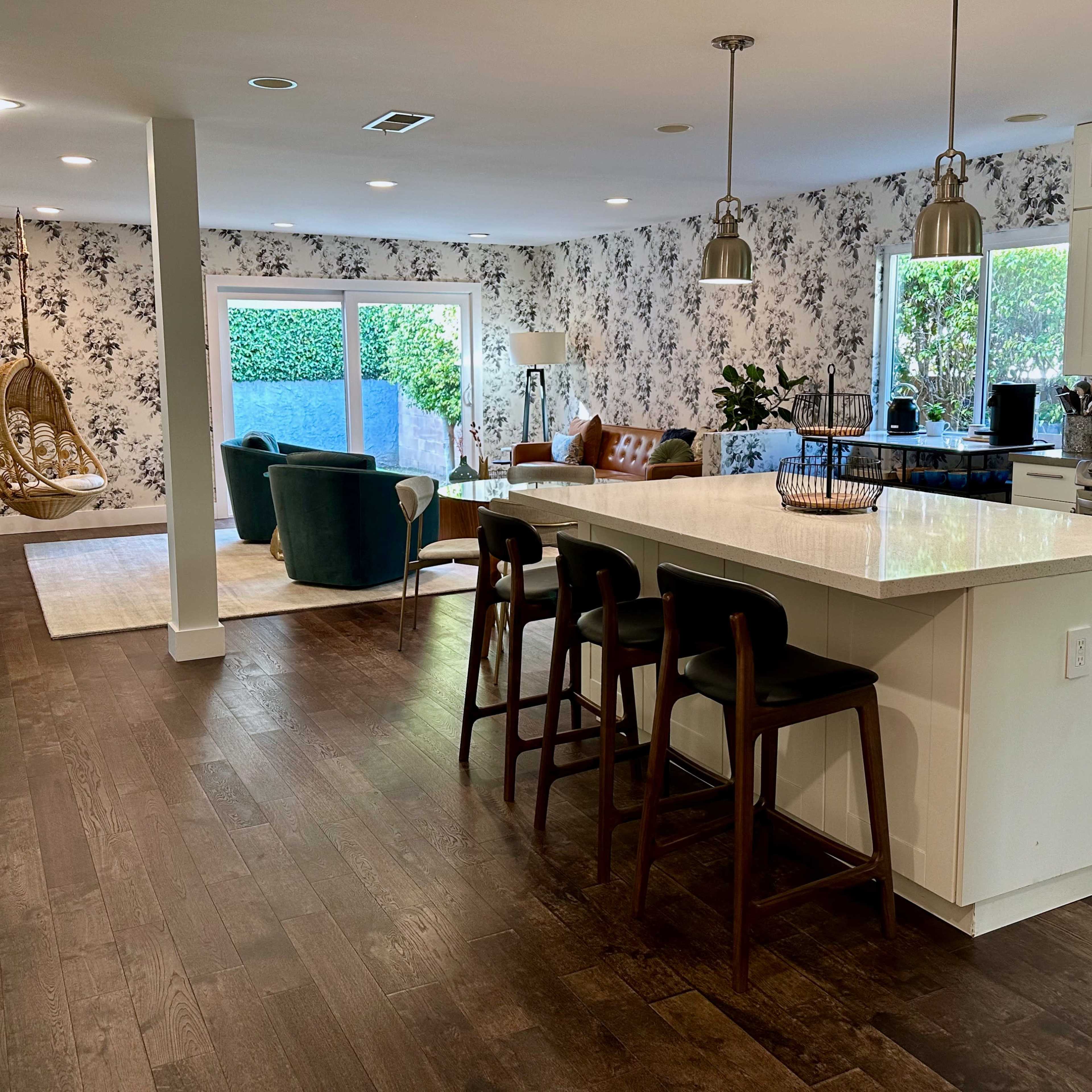 A modern open-concept living space with a kitchen bar, a dining area, and a cozy lounge area featuring a hanging chair and floral wallpaper.