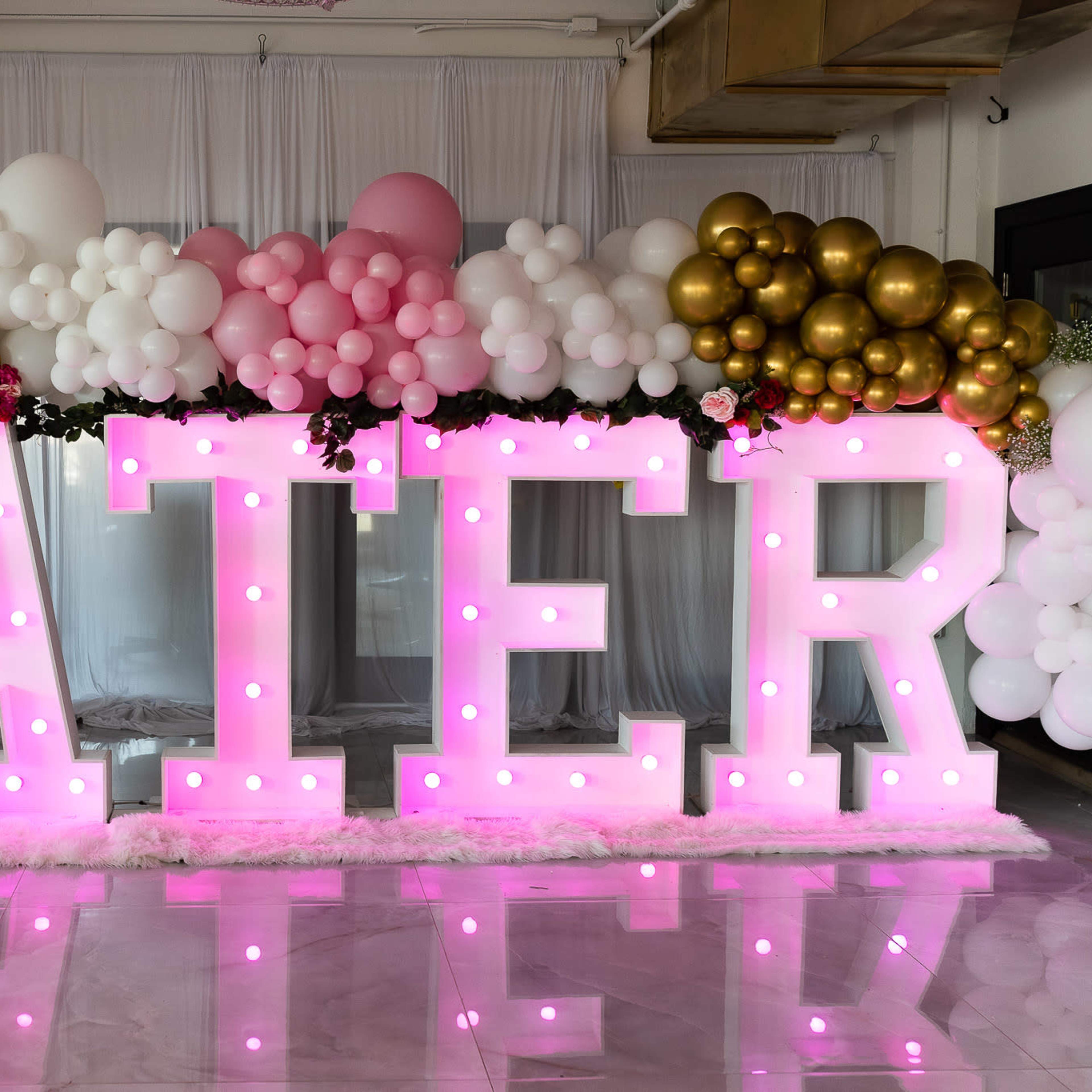 Large illuminated letters spelling "CATER" surrounded by colorful balloons in a decorated indoor setting.