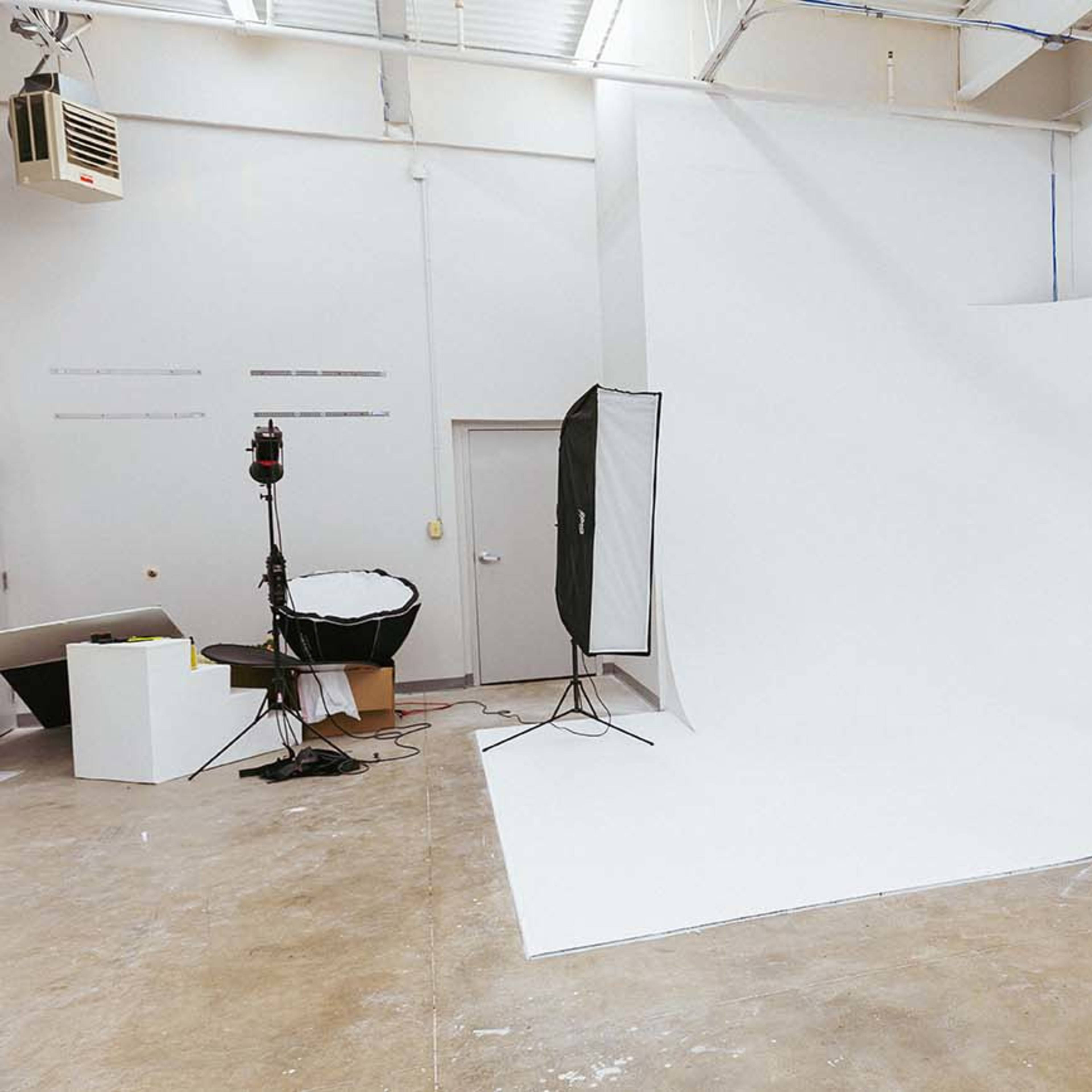 A photography studio with a large white backdrop, lighting equipment, and a few props arranged on the floor.