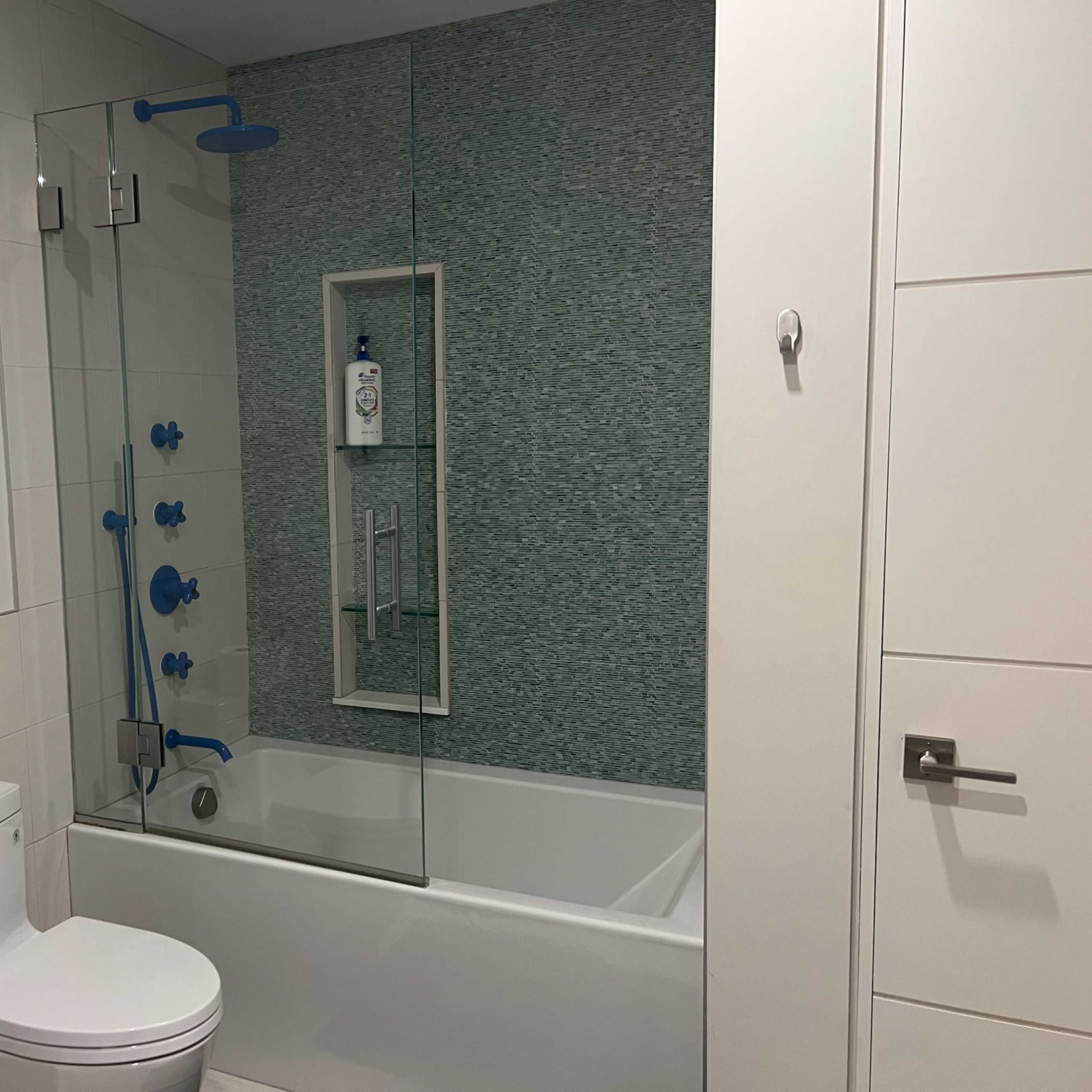 A bathroom featuring a bathtub with a glass partition, a toilet, and a blue and white tiled wall.