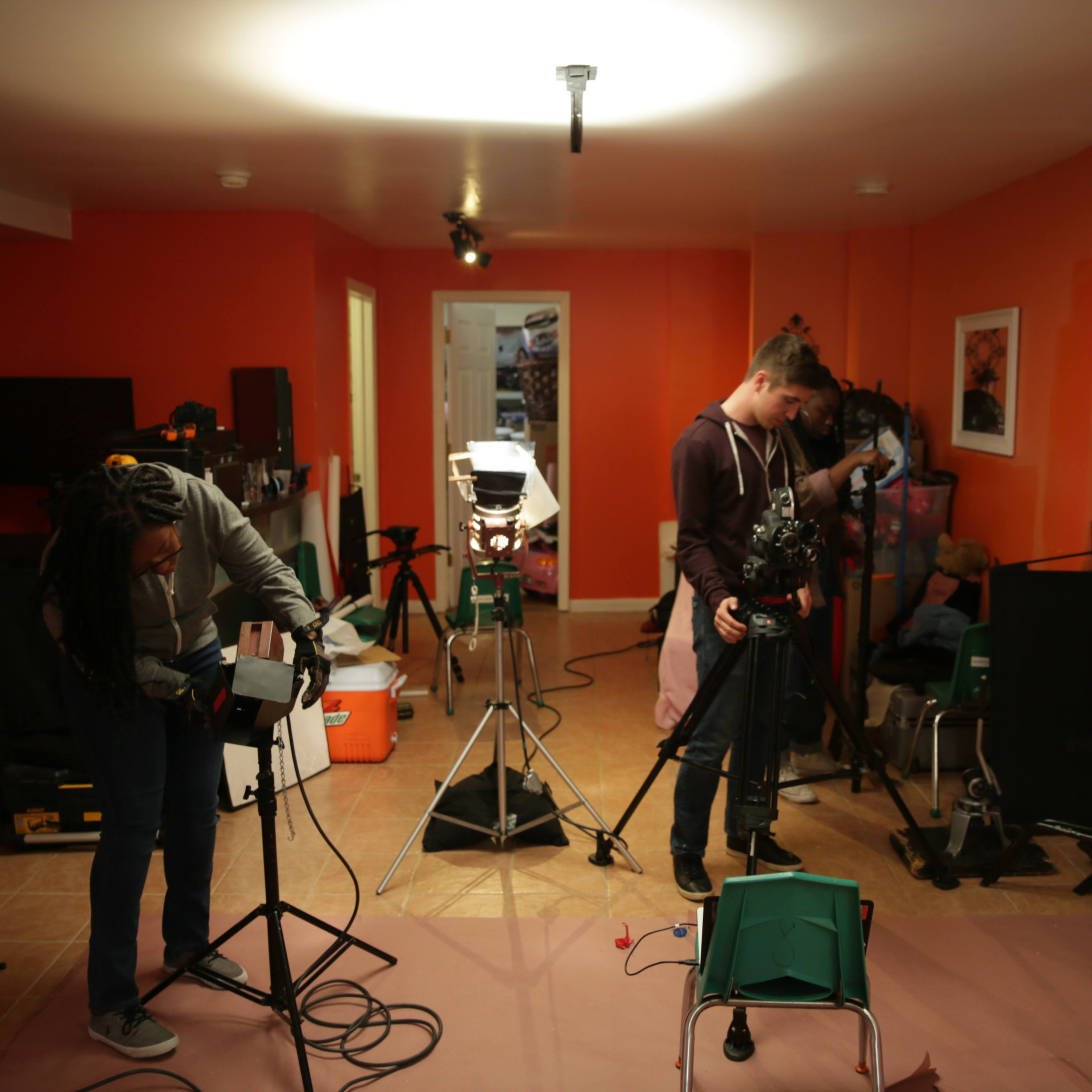 Two individuals are setting up filming equipment in a brightly colored room.