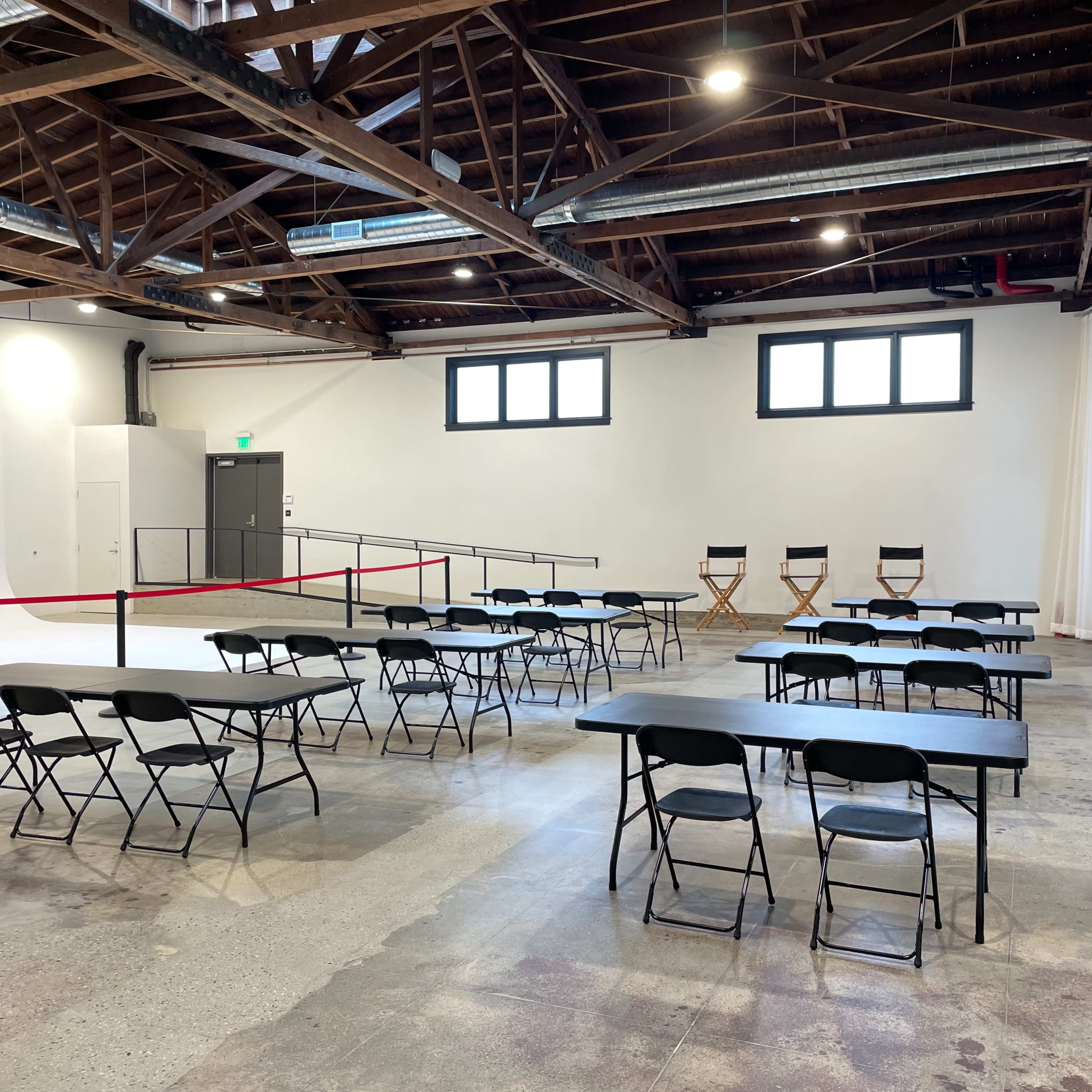 A spacious room with several rows of black folding tables and chairs, along with three director's chairs against one wall.