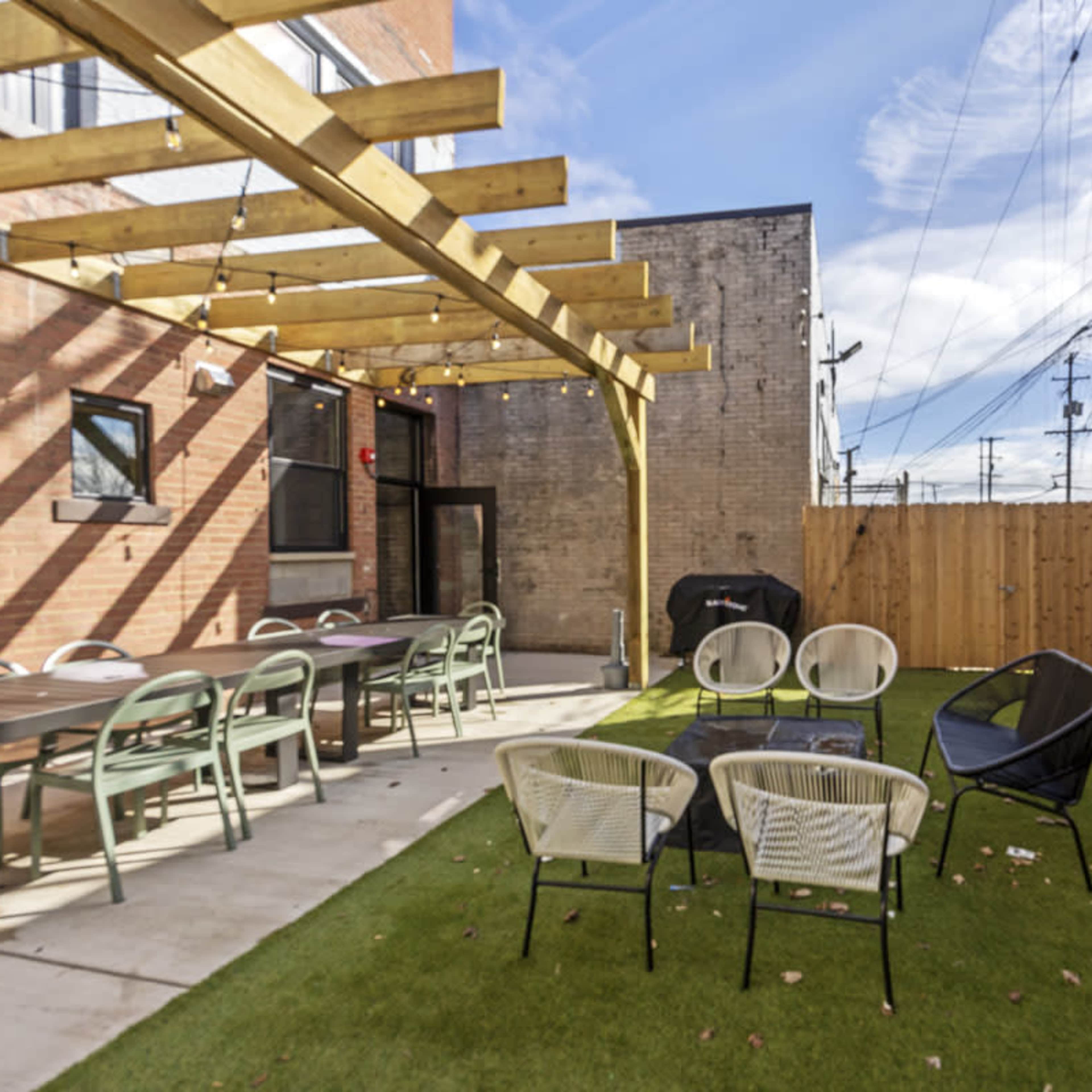 An outdoor patio area with a wooden pergola, seating arrangements, and a grassy surface surrounded by brick walls.