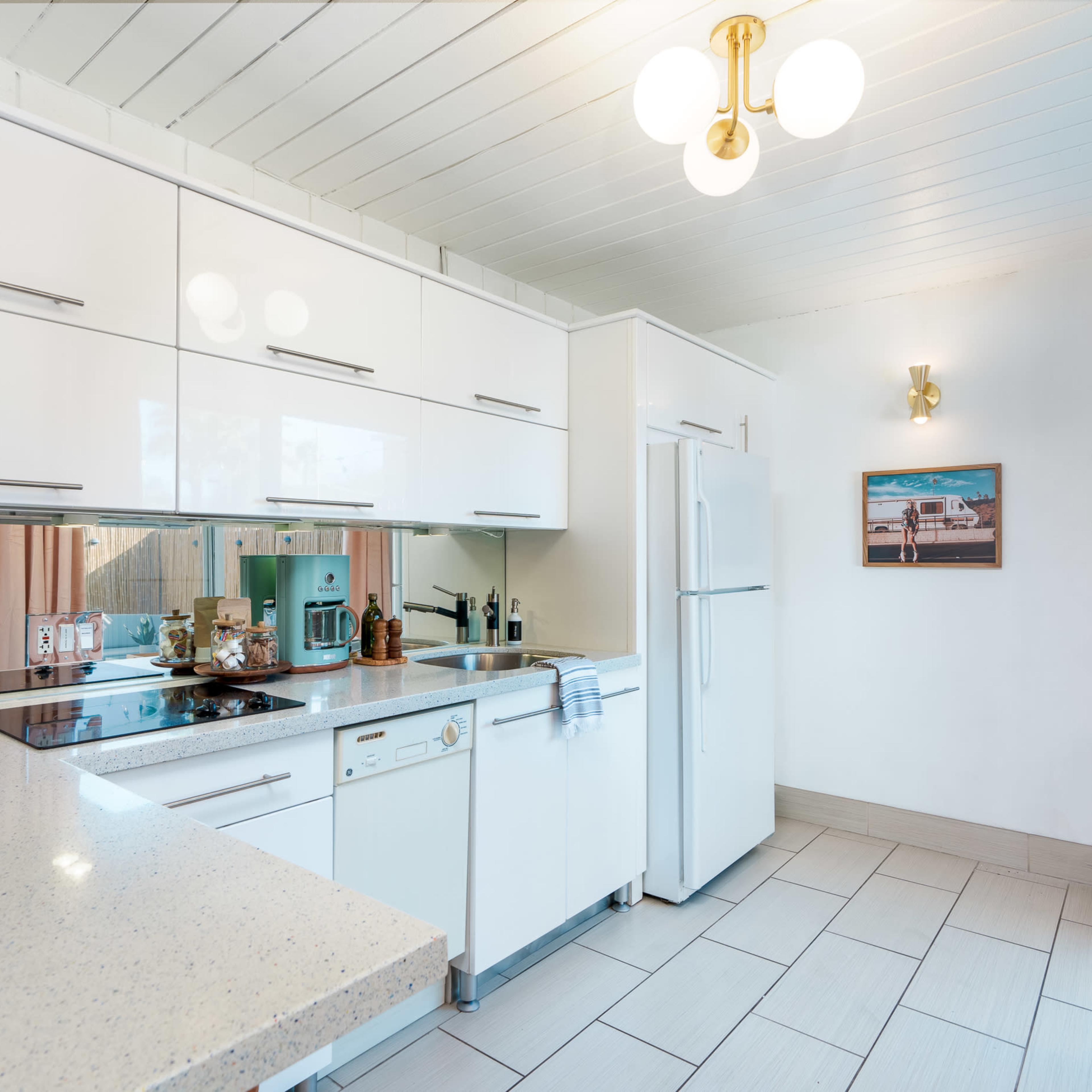 A modern kitchen with white cabinets, a countertop, and stainless steel appliances, featuring a beige tile floor and a light fixture on the ceiling.