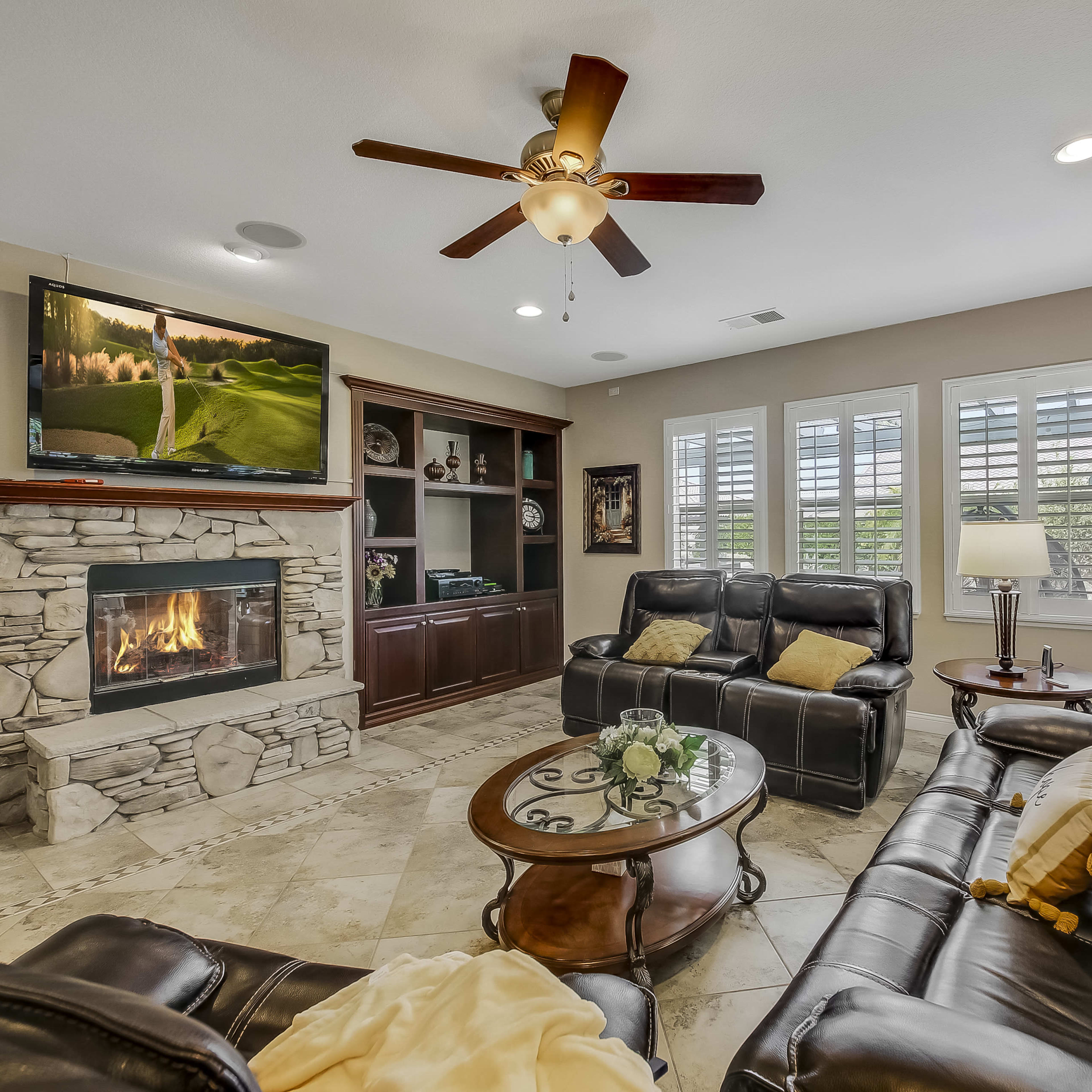 A living room with a stone fireplace, a large television mounted above it, and leather sofas arranged around a circular coffee table.
