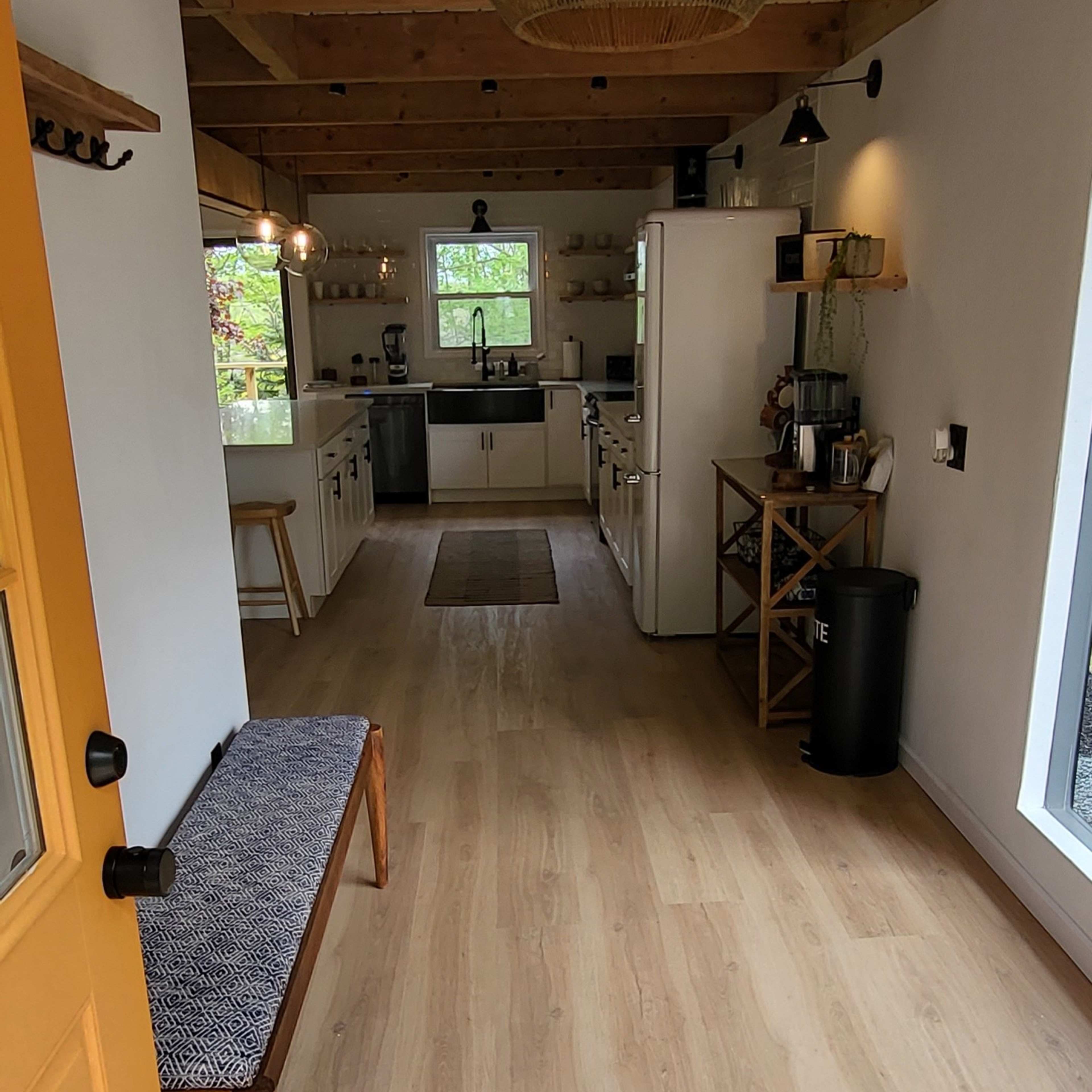 A brightly lit, modern interior of a kitchen and living area featuring wooden beams, a yellow door, and a bench along the wall.