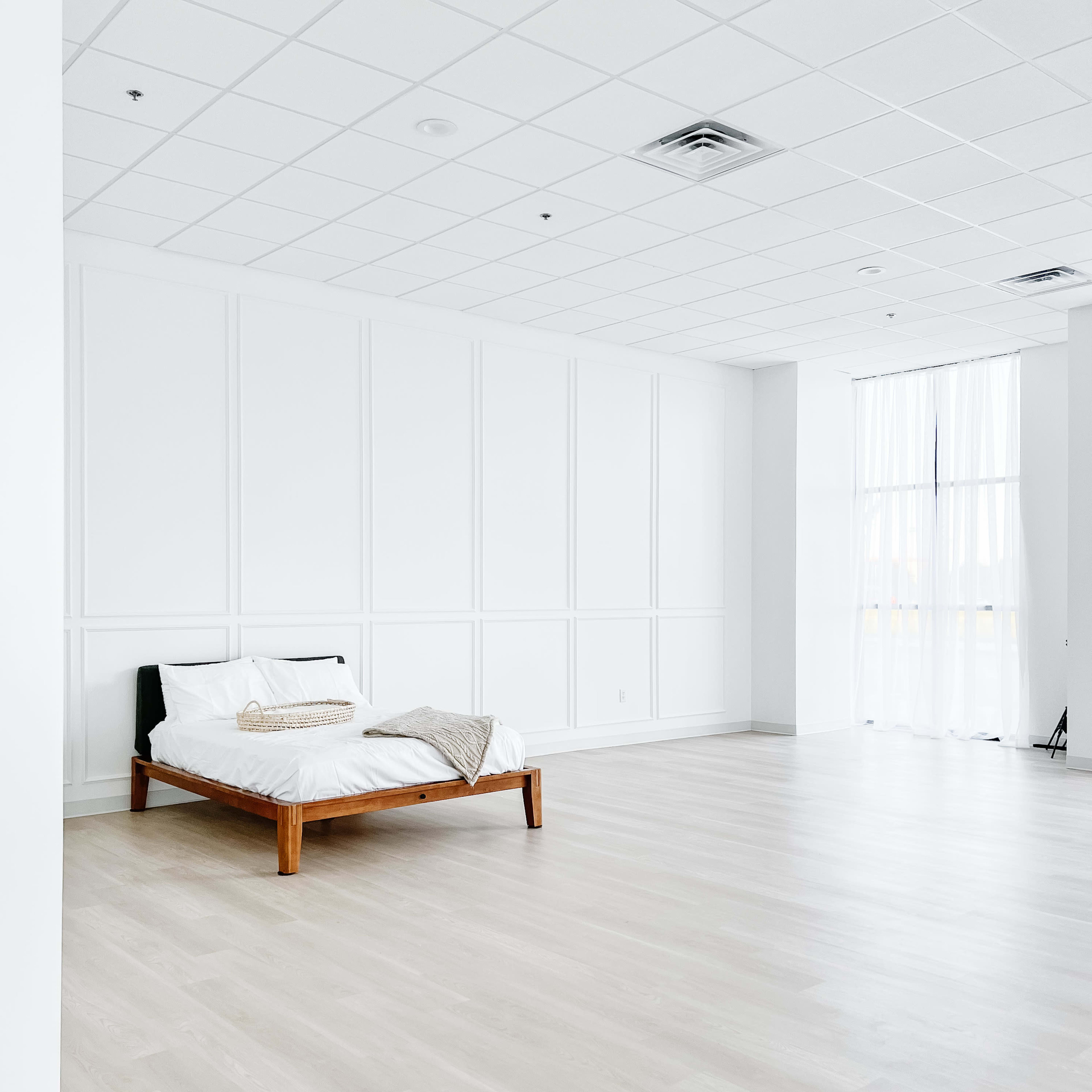 A spacious, minimalistic bedroom with a wooden bed frame positioned against a plain white wall.