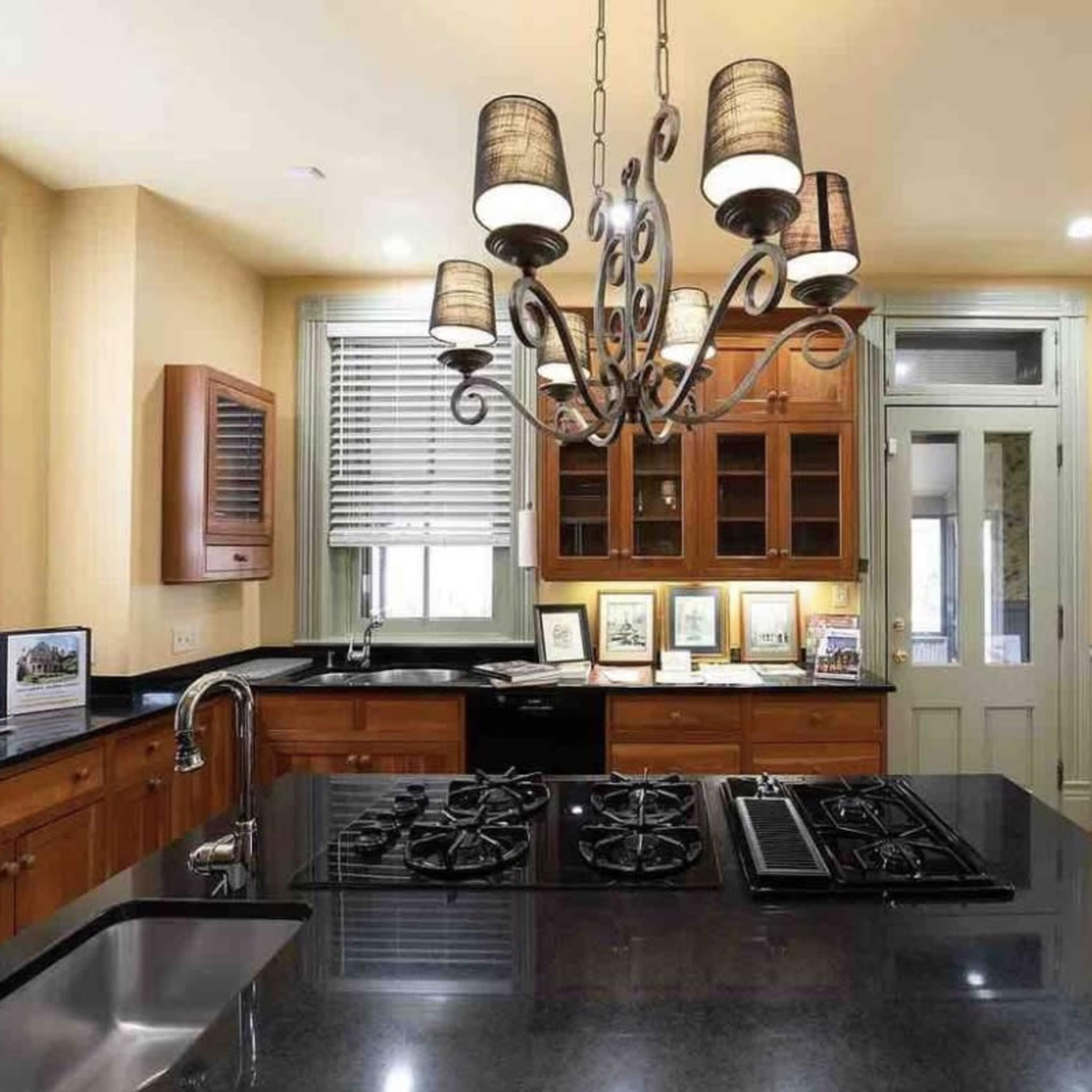 The room features a light green wall with a chandelier, a fireplace with a mirror above it, and a cozy seating area with two sofas and a round table.