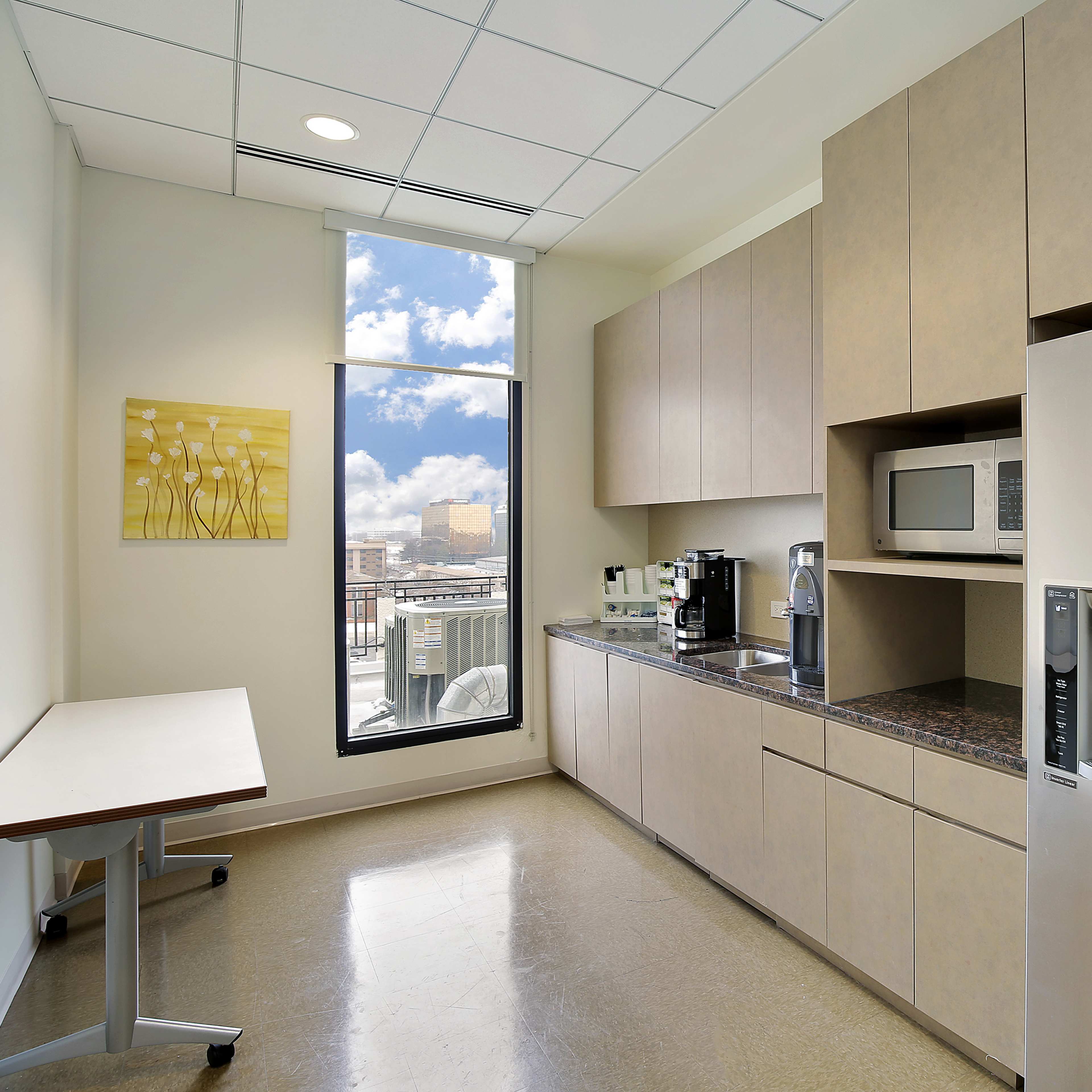 A modern kitchen with beige cabinetry, a countertop, and large windows letting in natural light.