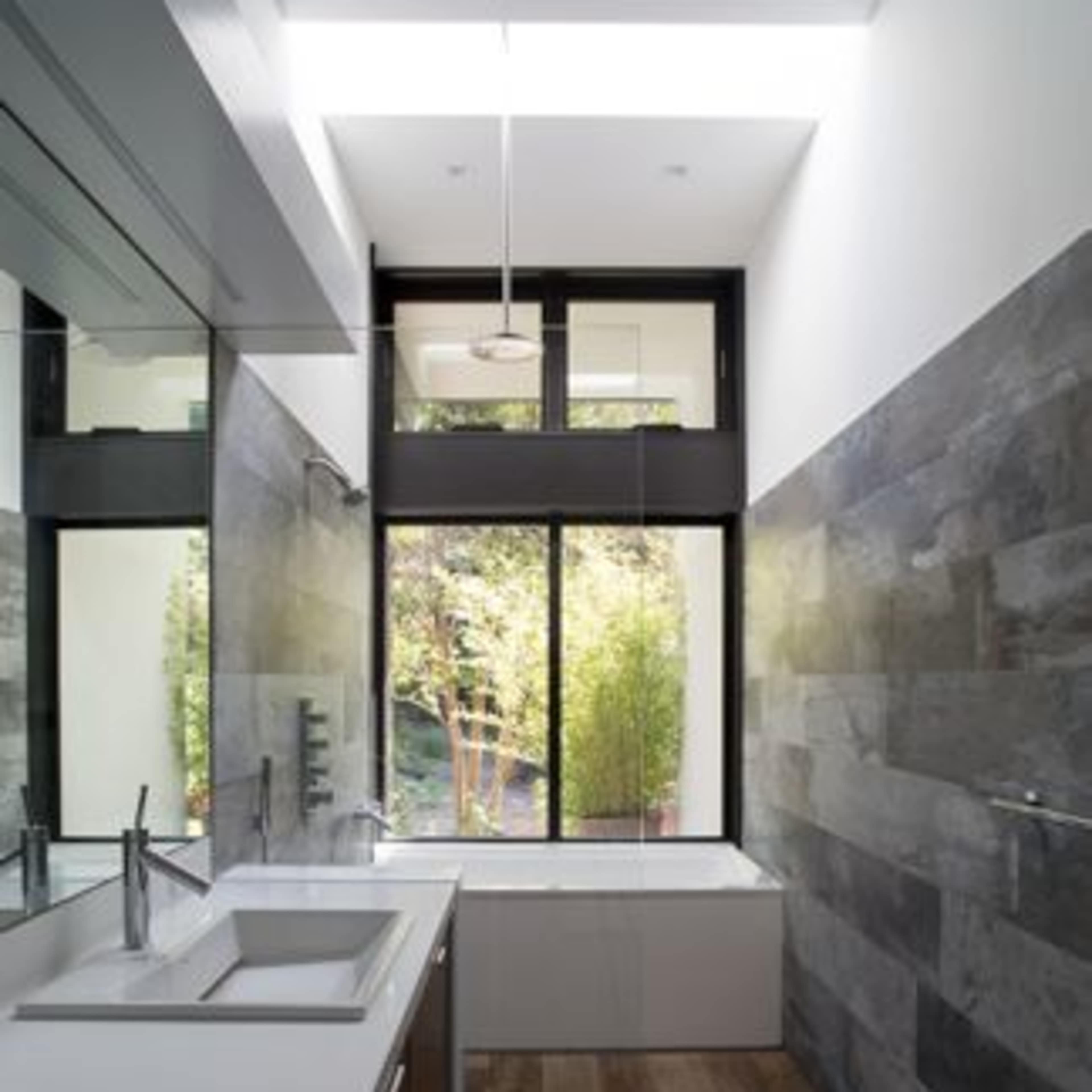 A modern bathroom features dual sinks, sleek cabinetry, and large windows that provide natural light and a view of greenery outside.