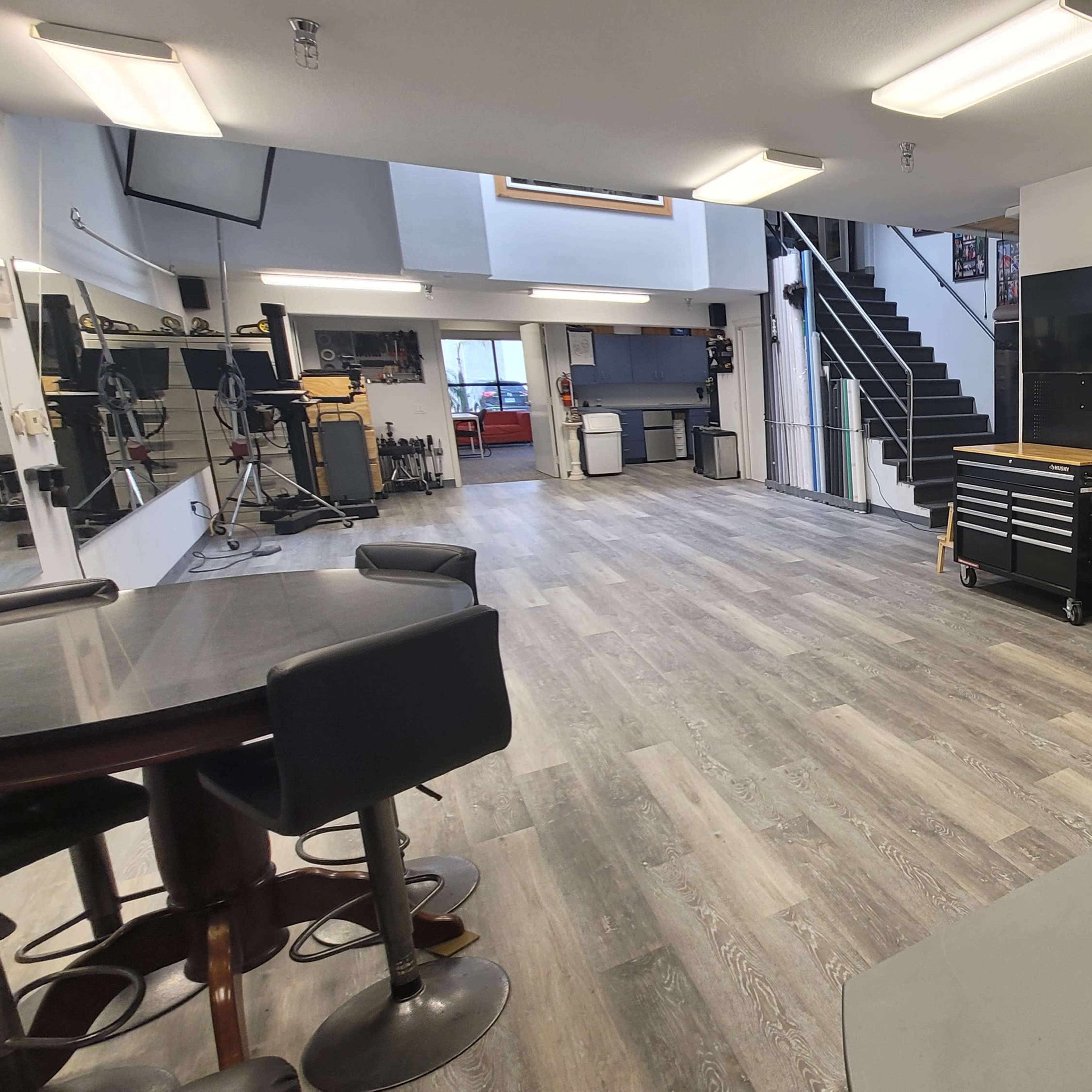 A spacious, modern studio with a kitchen area, workstations, and a staircase in the background.