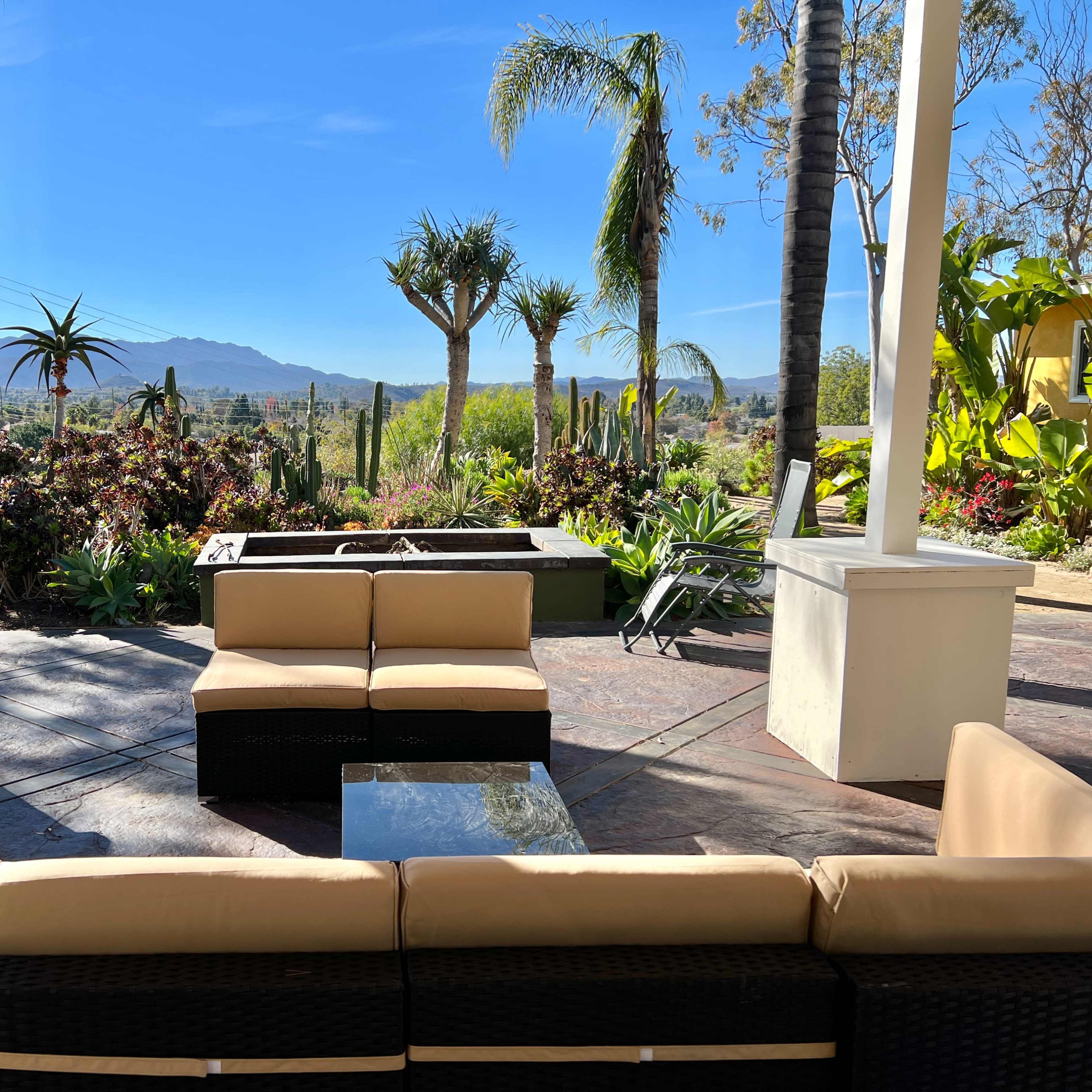 A patio area with a sectional sofa facing a view of mountains and landscaped gardens.