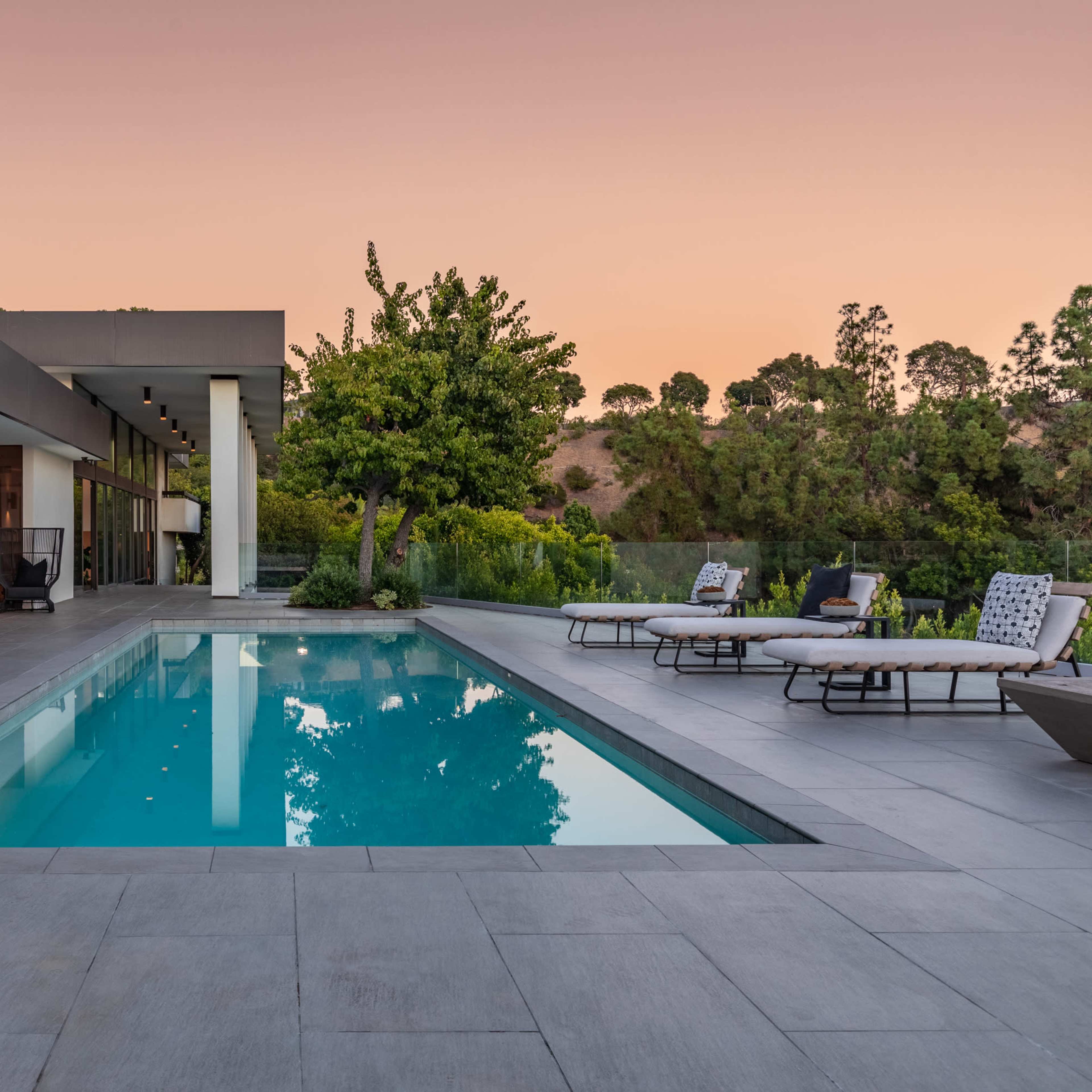 A modern house with a swimming pool and outdoor seating area is shown against a sunset backdrop.