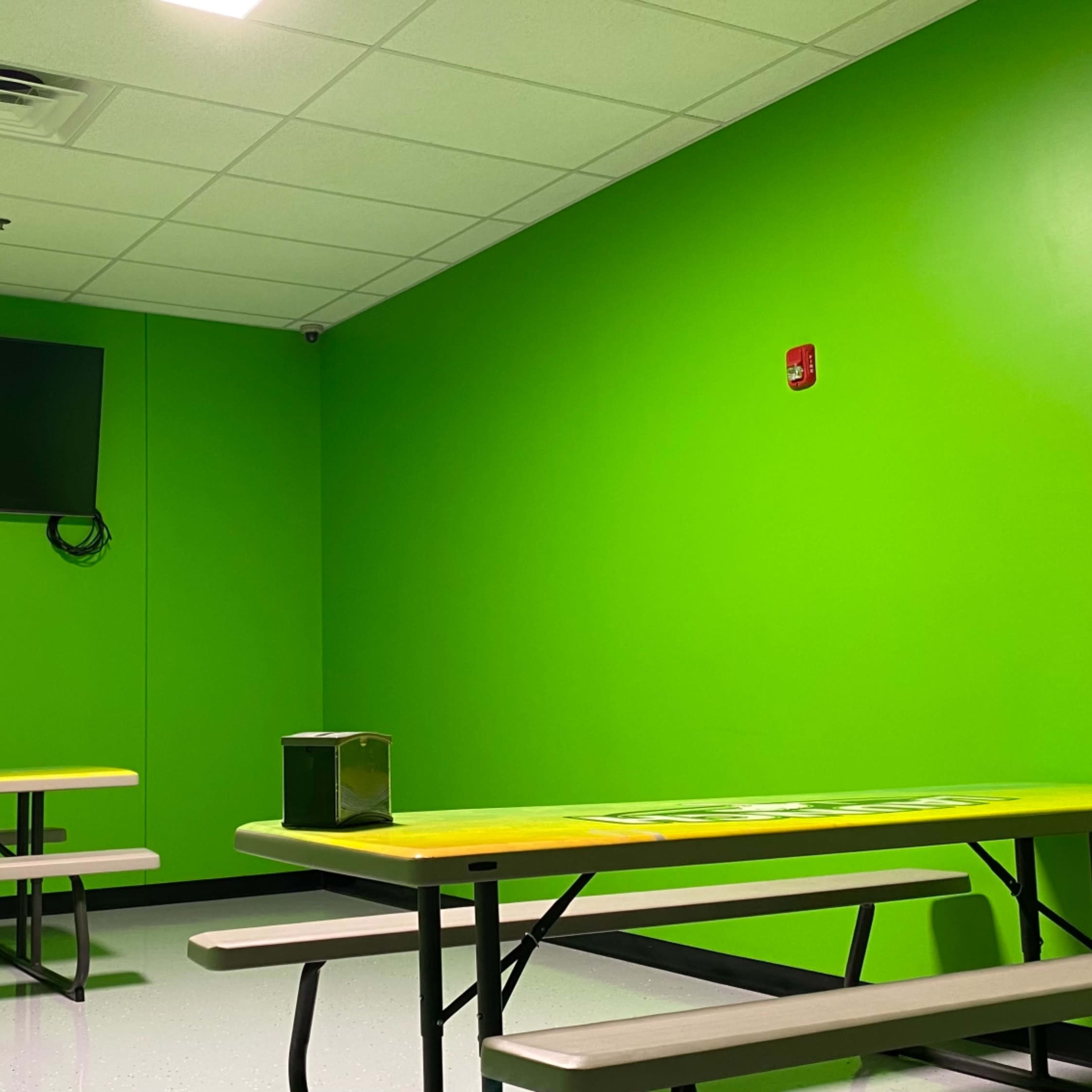 A brightly colored green room with two yellow-topped tables and a wall-mounted television.
