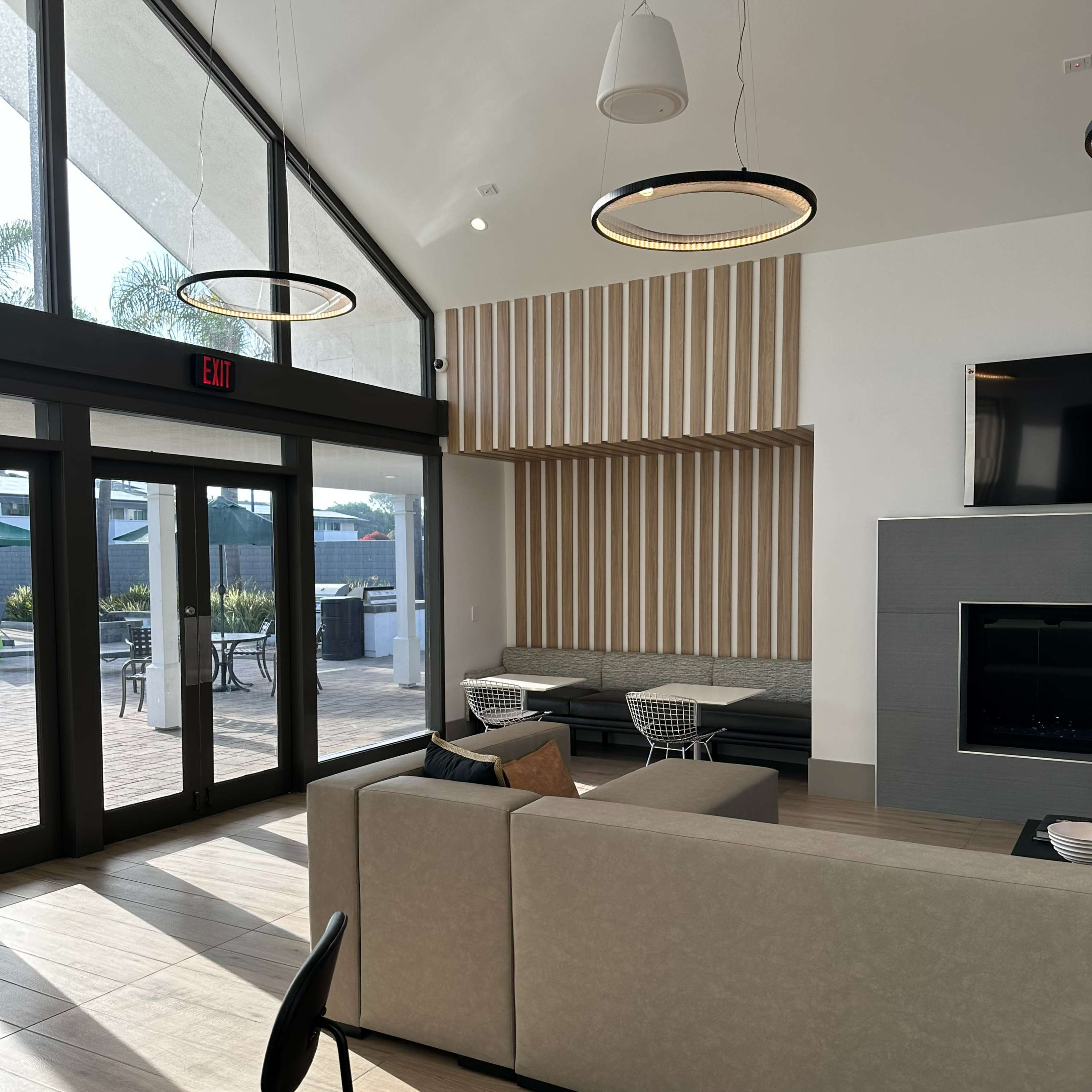 A modern lounge area with large windows, a wall adorned with wooden panels, a sectional sofa, and a fireplace.