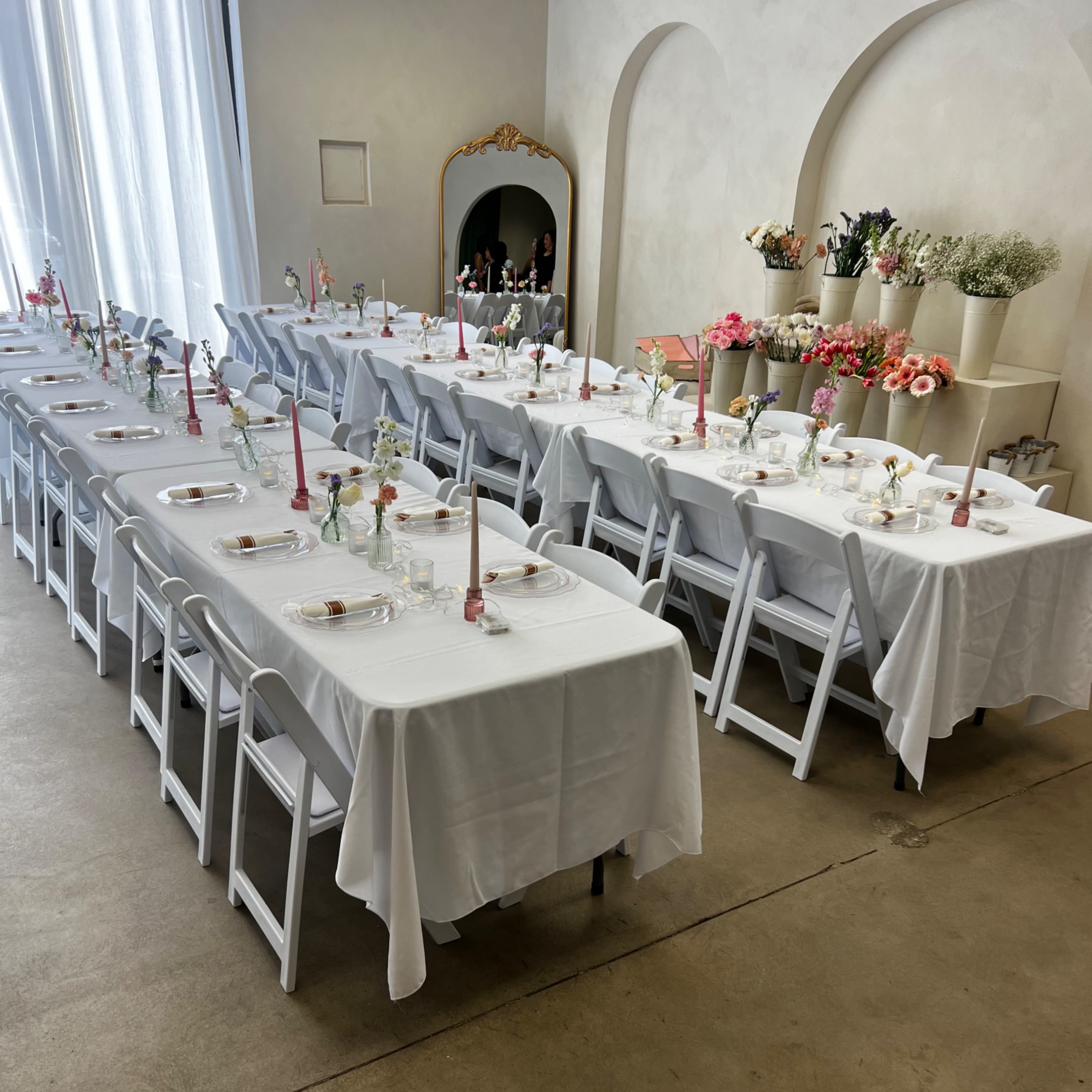 A neatly arranged dining room with multiple long tables set with white tablecloths, candles, and flower arrangements.