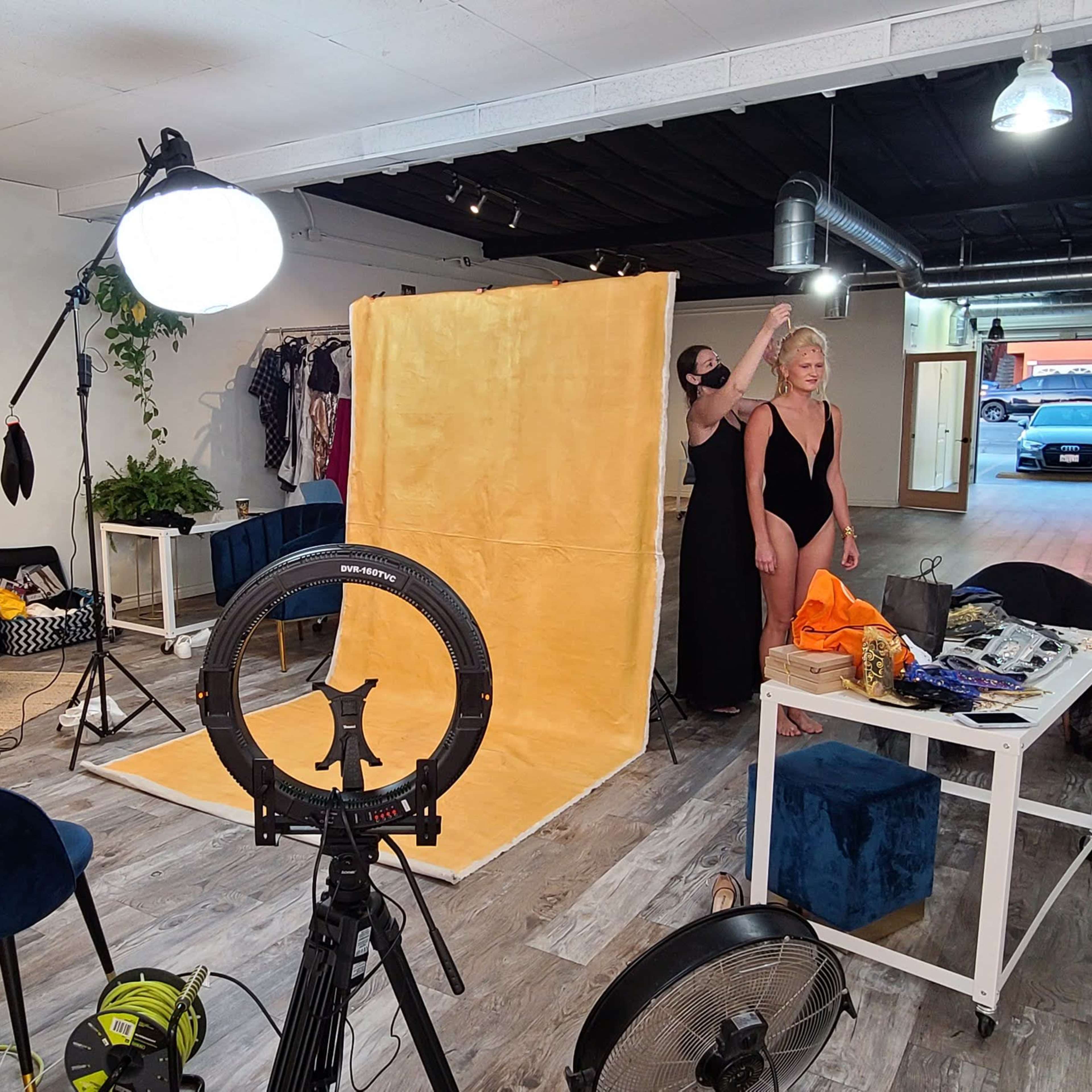 A photography studio with a large yellow backdrop, lighting equipment, and a model preparing for a photo shoot.