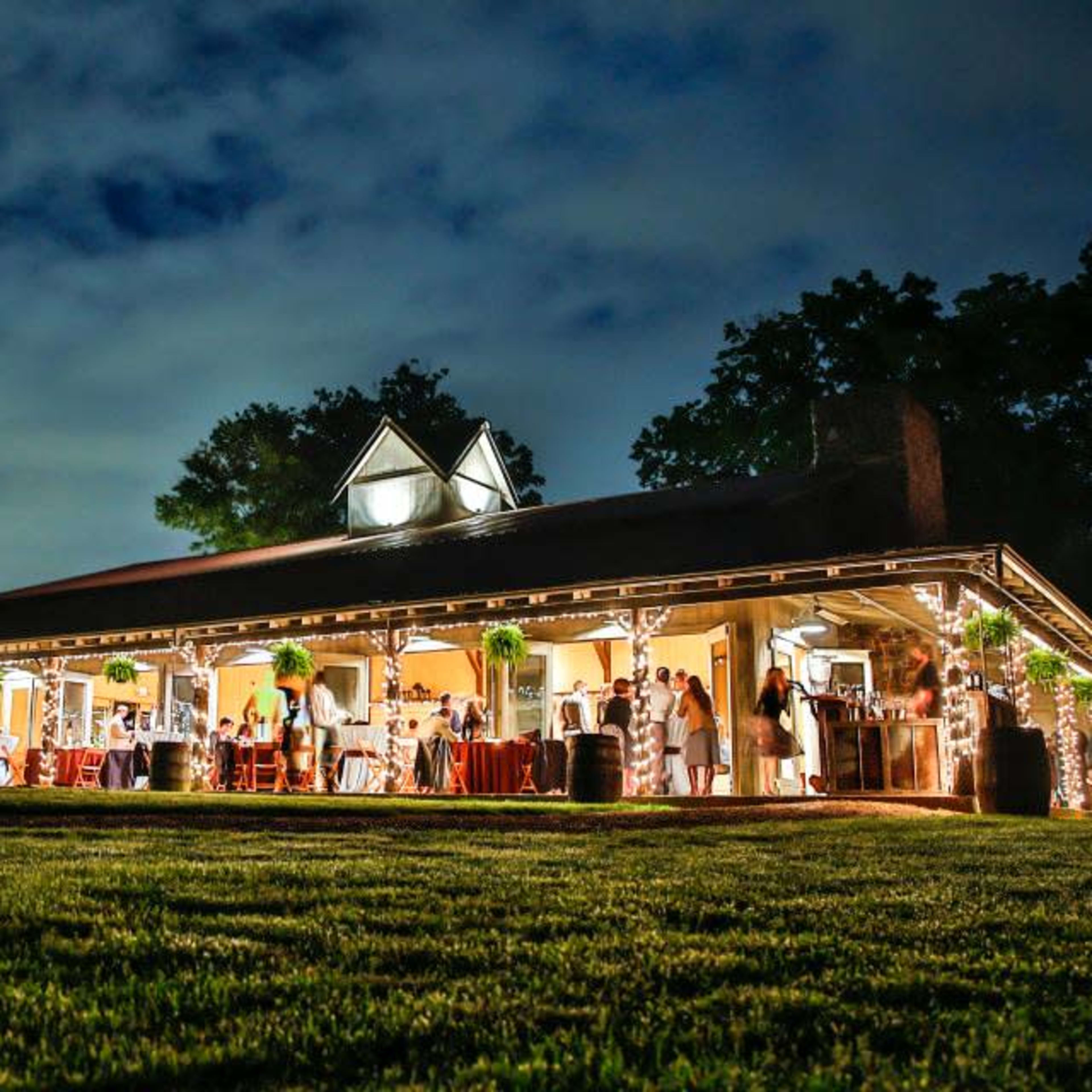 A large, well-lit building with a covered porch hosted a gathering of people in a grassy area under a cloudy sky.