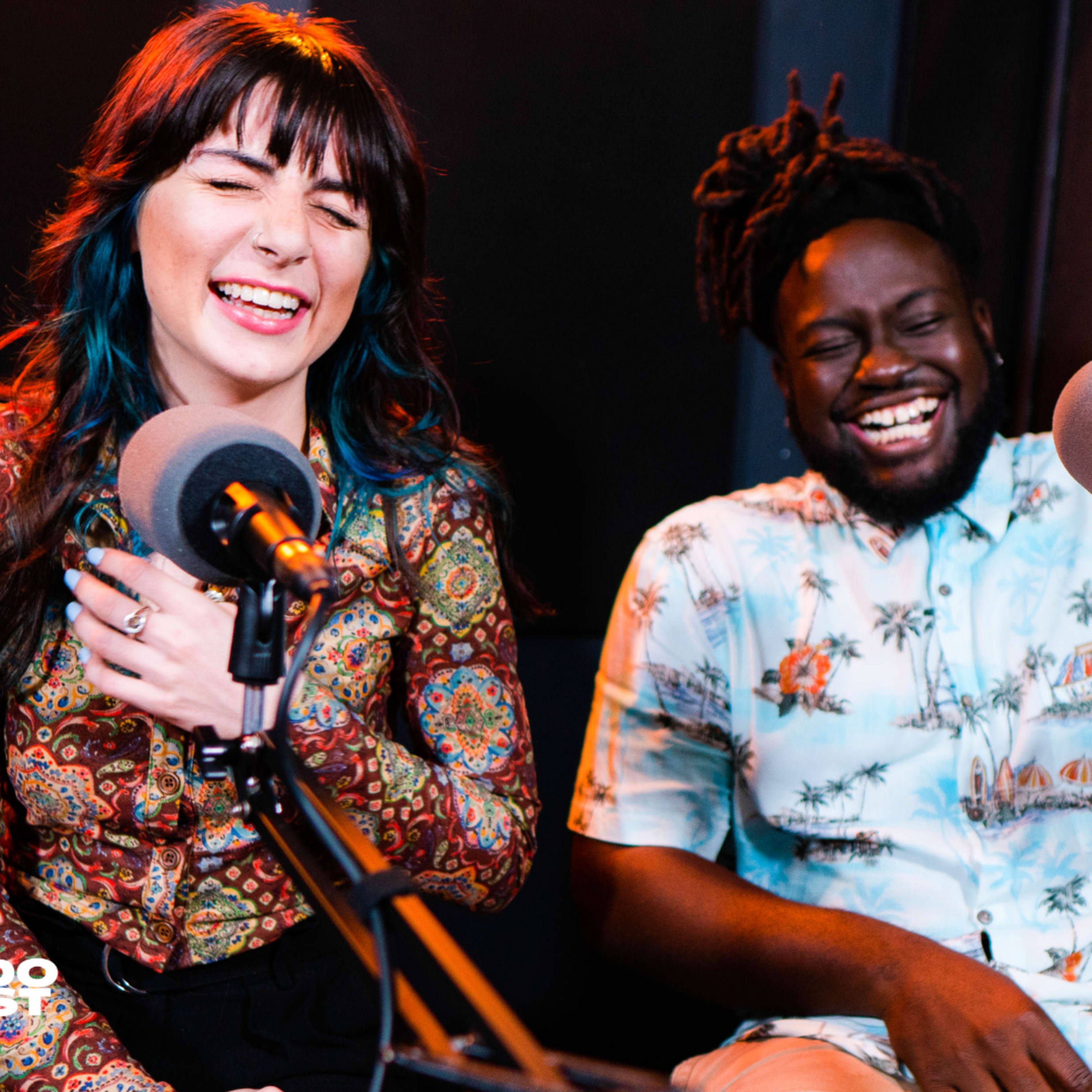 Two people sit in a podcast studio, laughing while speaking into microphones.