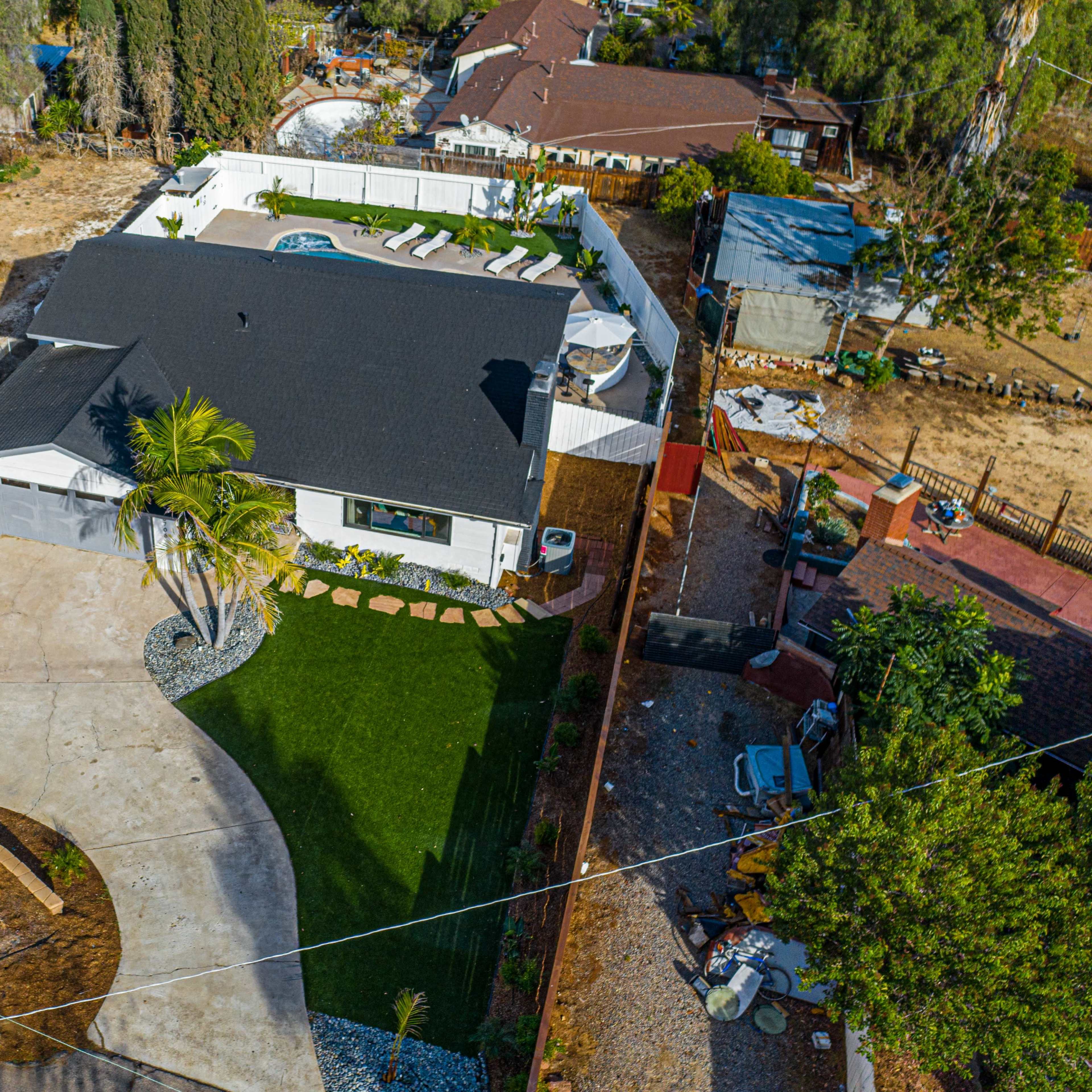 A modern single-story house with a landscaped yard, a circular driveway, and a backyard pool area surrounded by greenery.