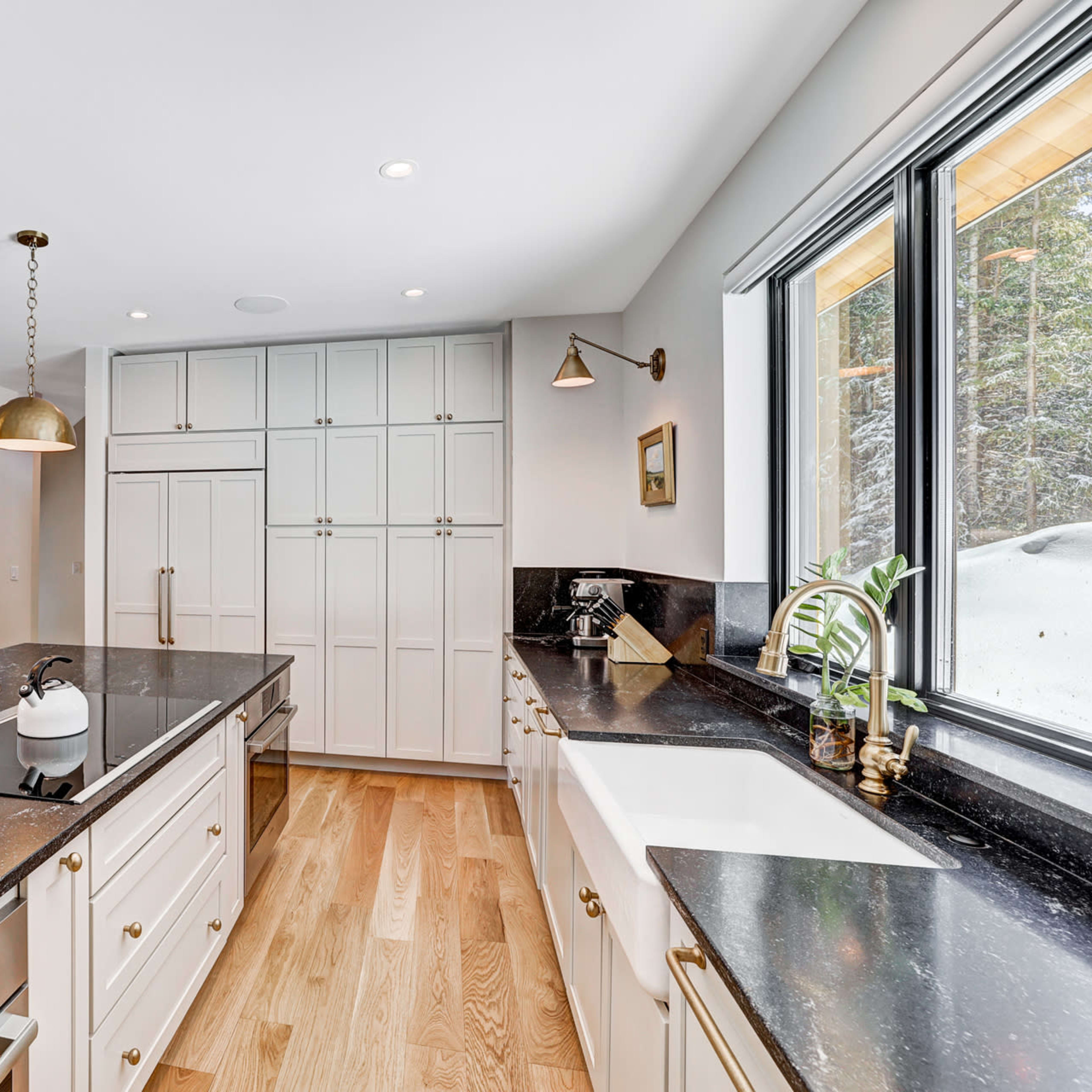 A modern kitchen features a large island with a dark countertop, white cabinetry, and brass pendant lights.