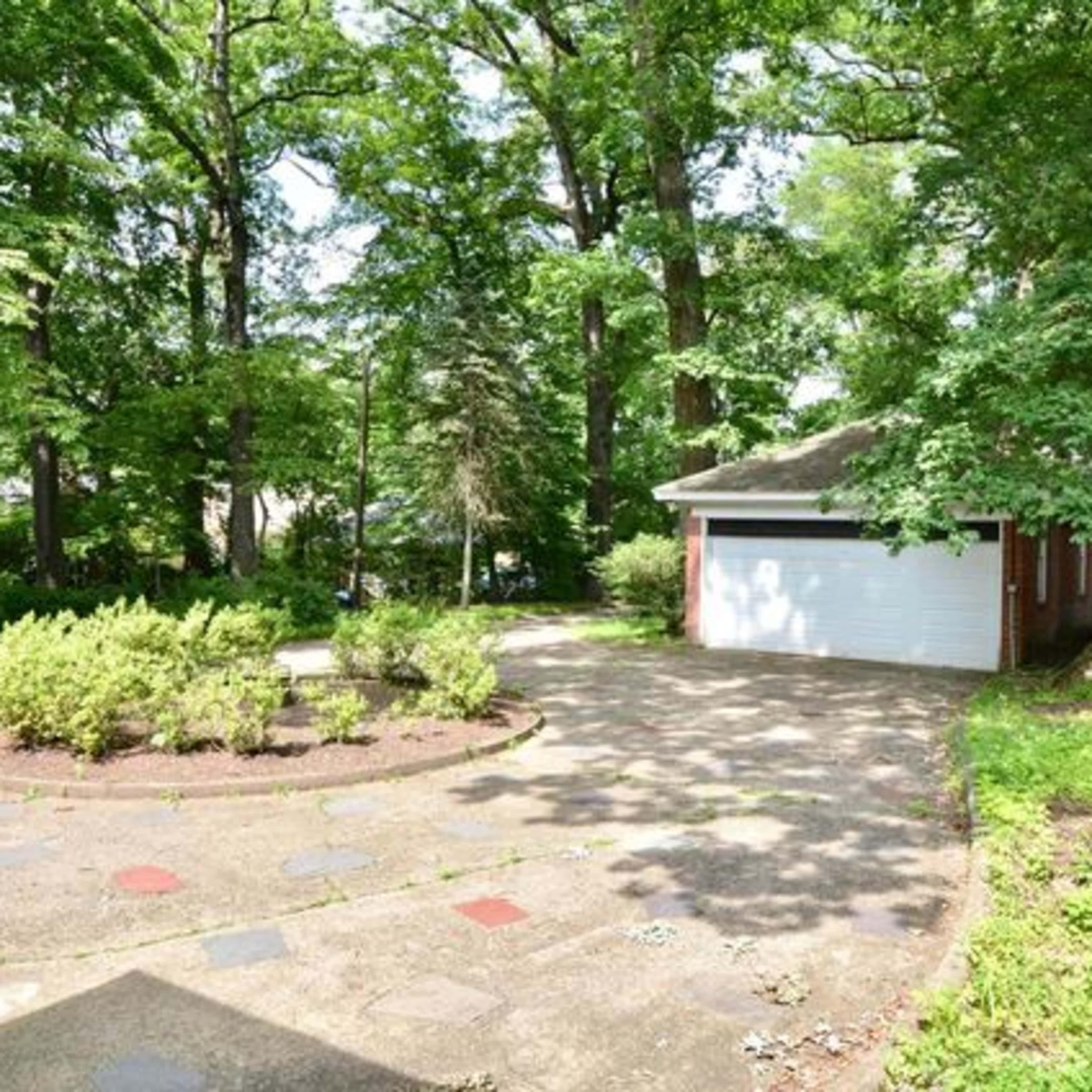 A paved driveway leading to a garage surrounded by trees and shrubs.