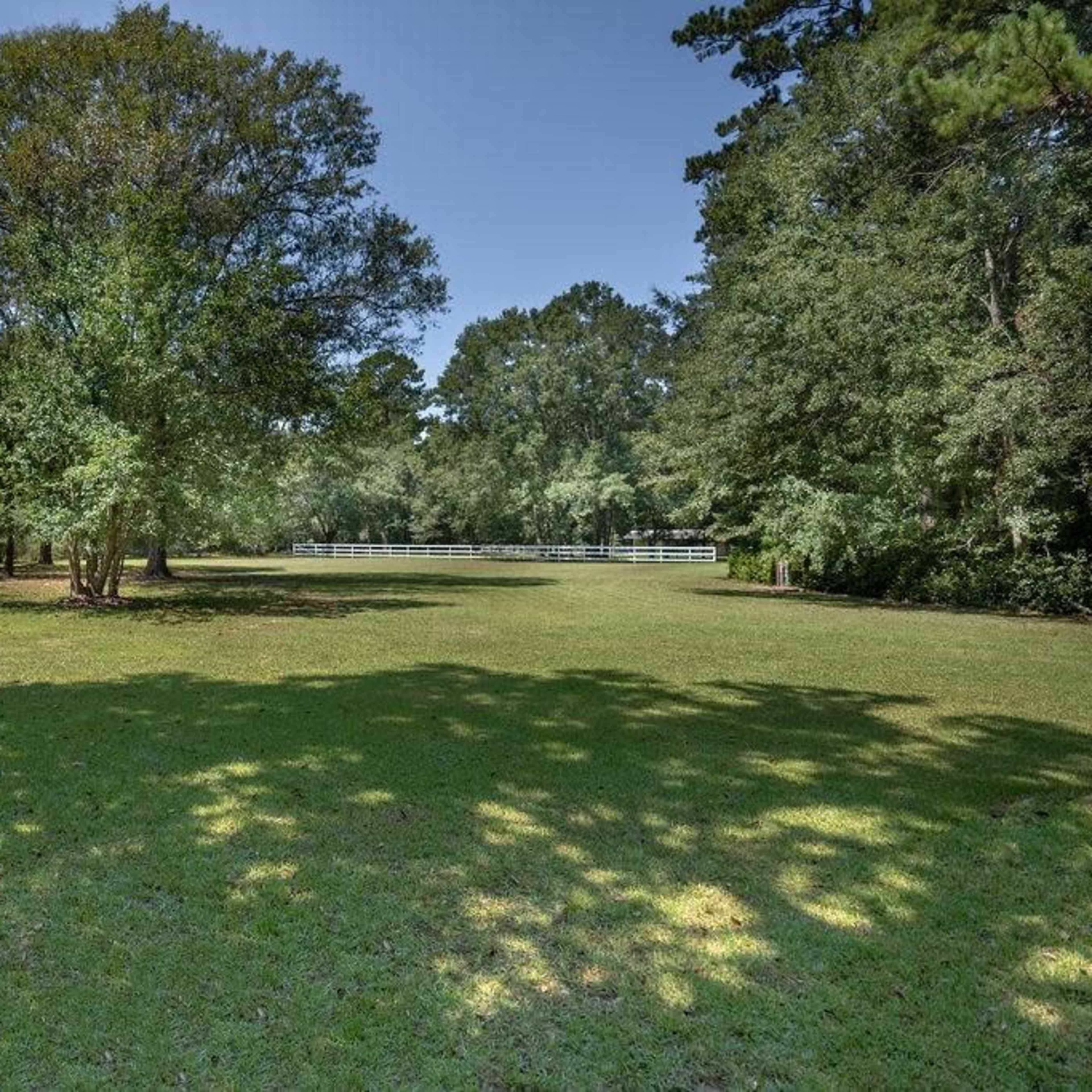A grassy area is surrounded by trees, with a white fence visible in the background.