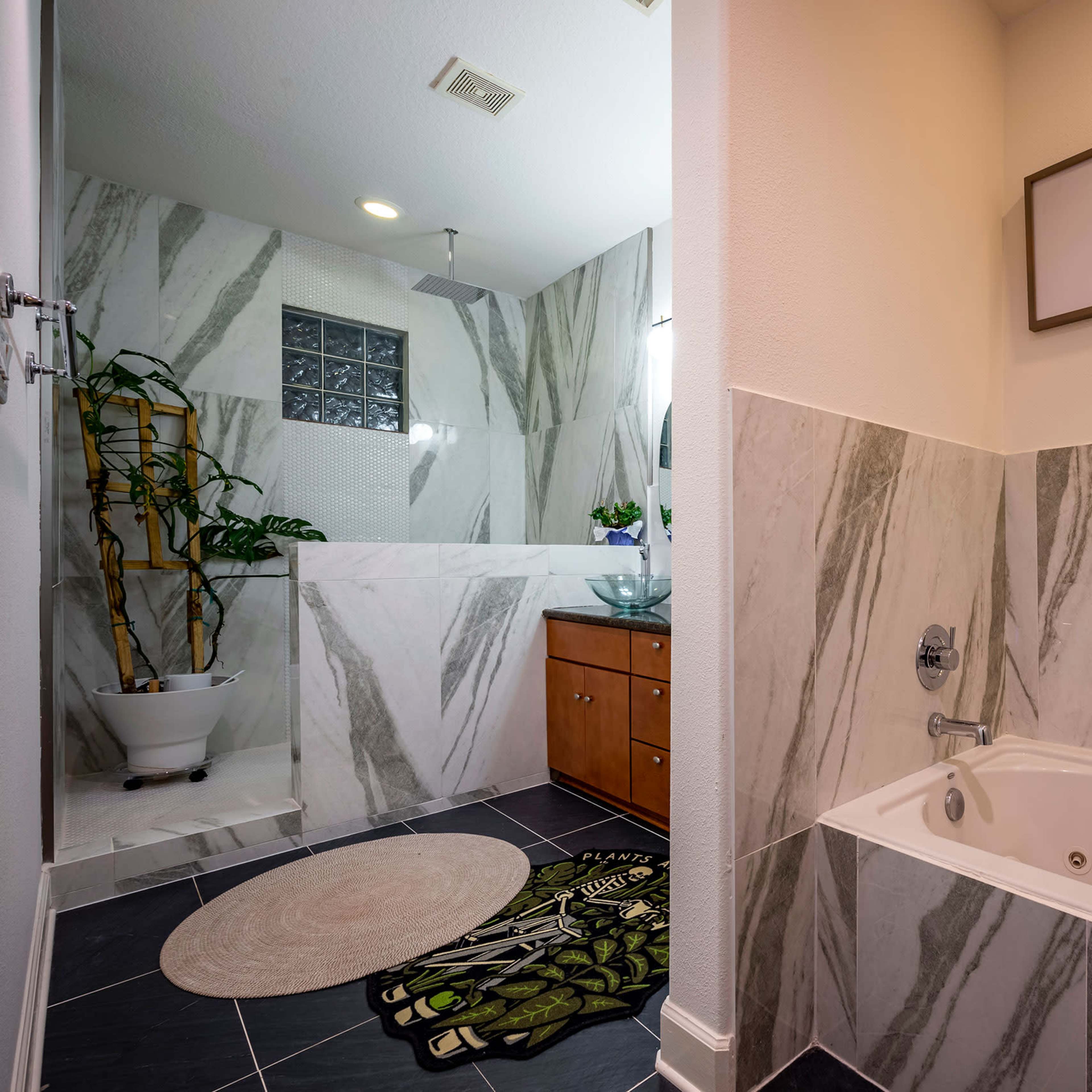 A modern bathroom featuring a glass block shower, a soaking tub with a decorative rug, and framed animal prints on the wall.