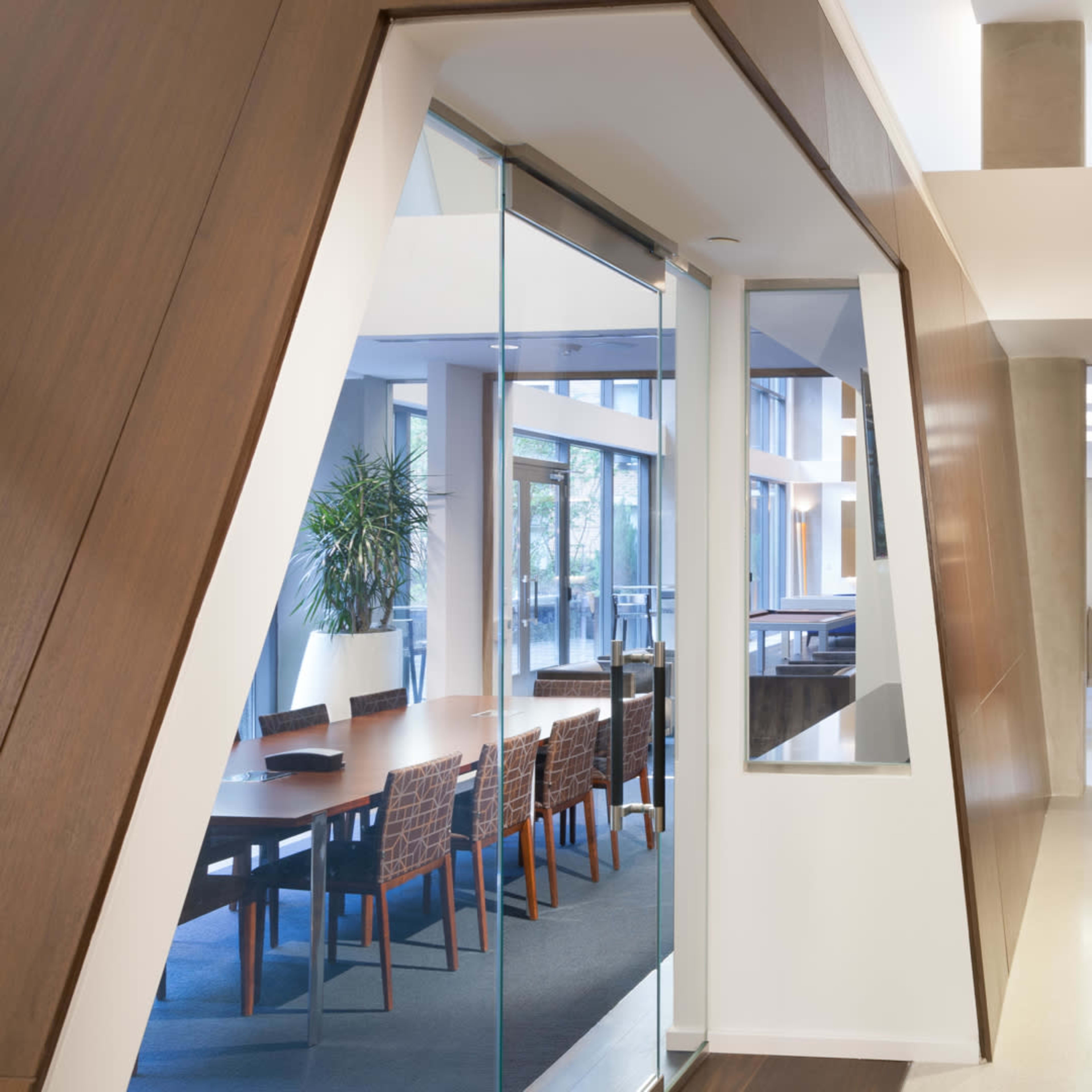 A modern interior hallway featuring large glass panels and wooden walls, leading towards a dining area in a spacious setting.