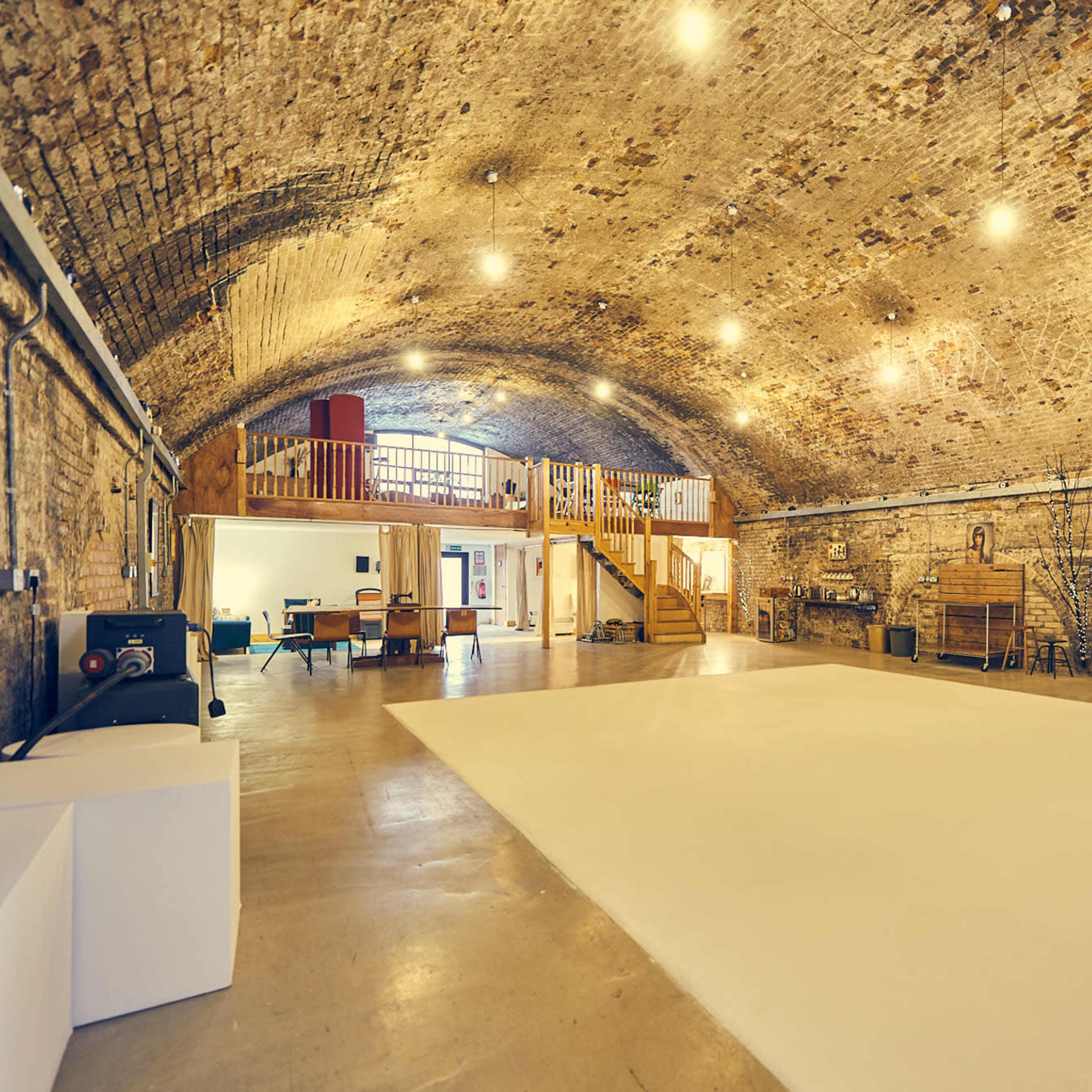 A spacious room with a high, arched brick ceiling, featuring a light-colored floor and various furnishings along the walls.
