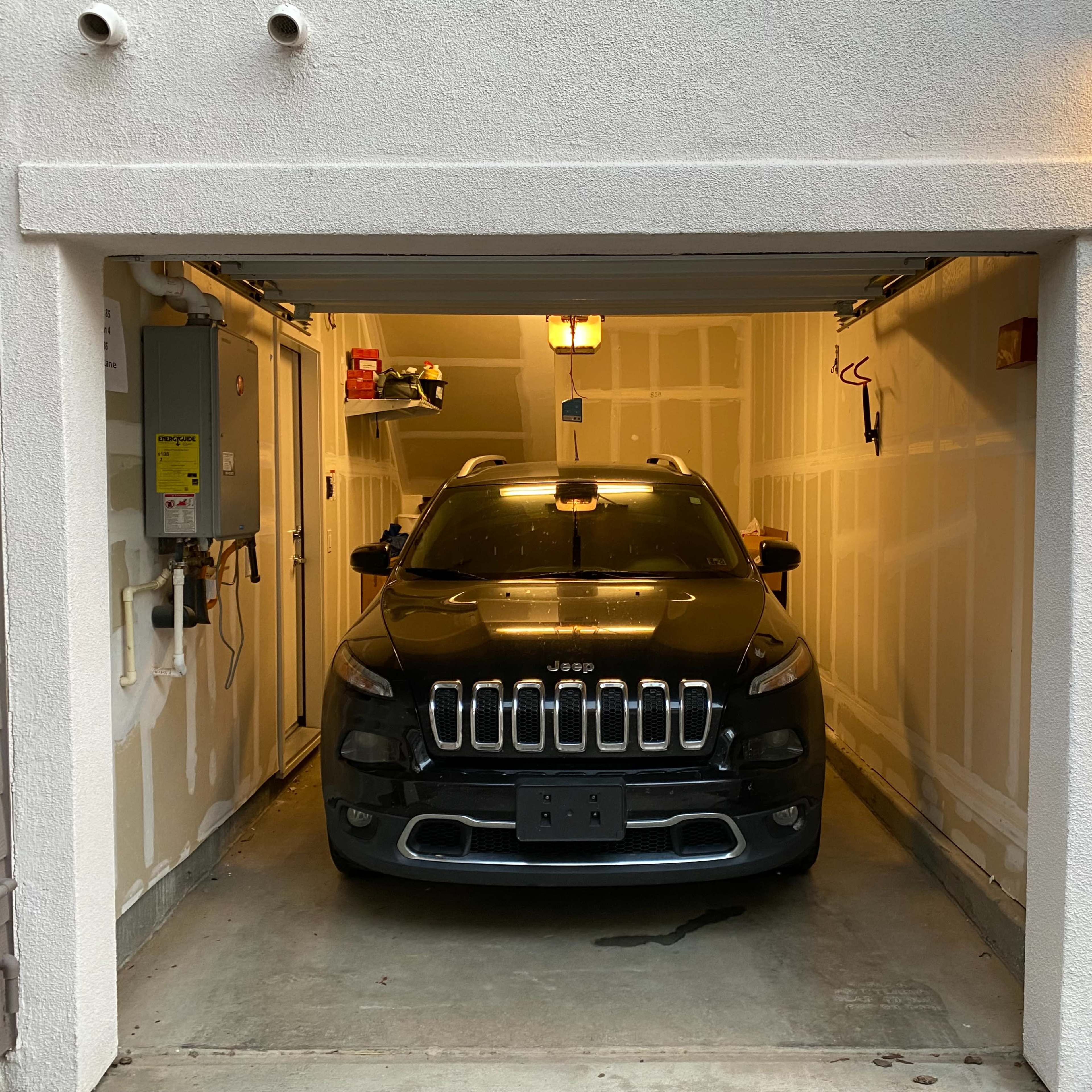 A black Jeep is parked inside a garage with partially finished walls and a utility panel on the side.