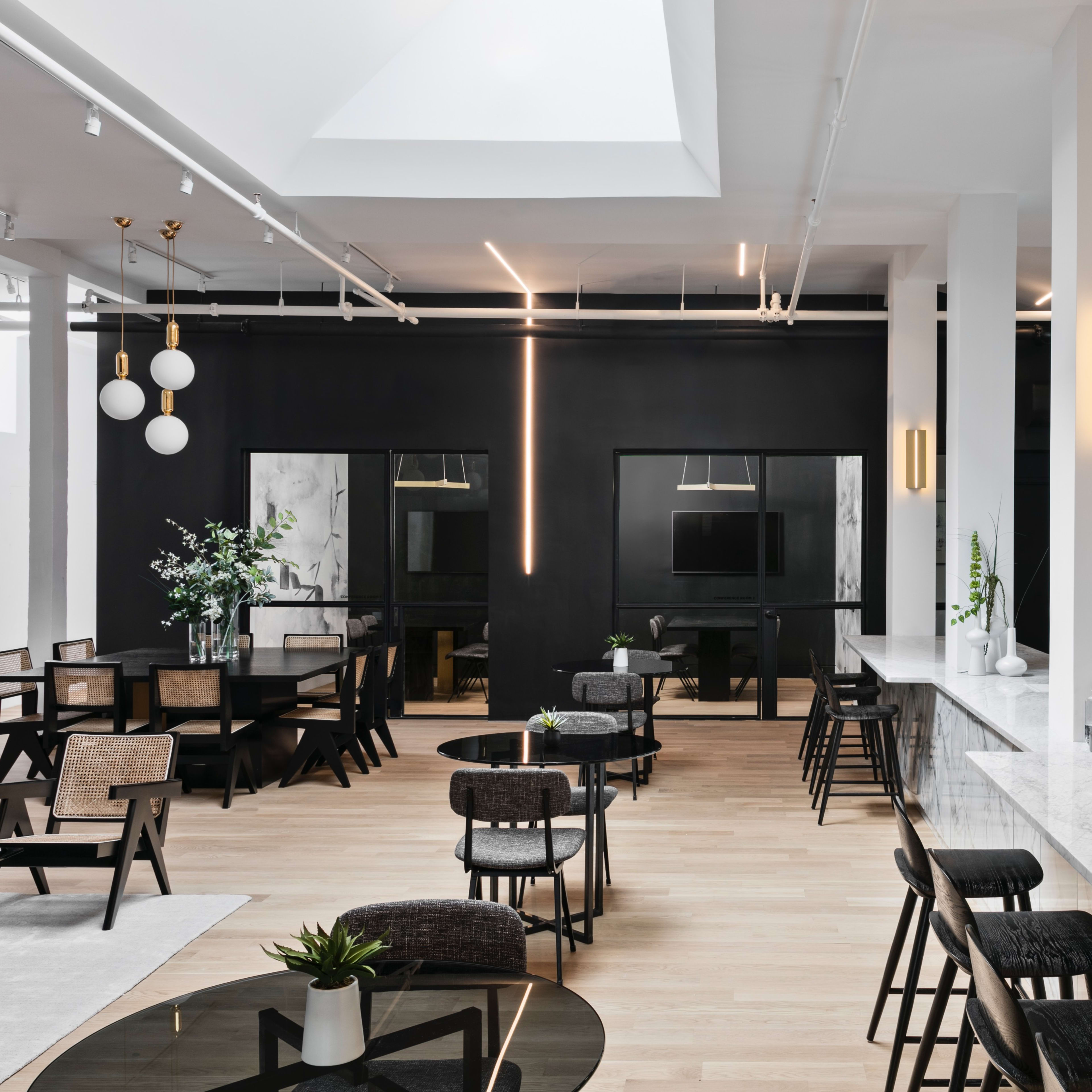 A sleek, contemporary interior features a mix of dining and seating areas with dark accents, marble surfaces, and ample natural light.
