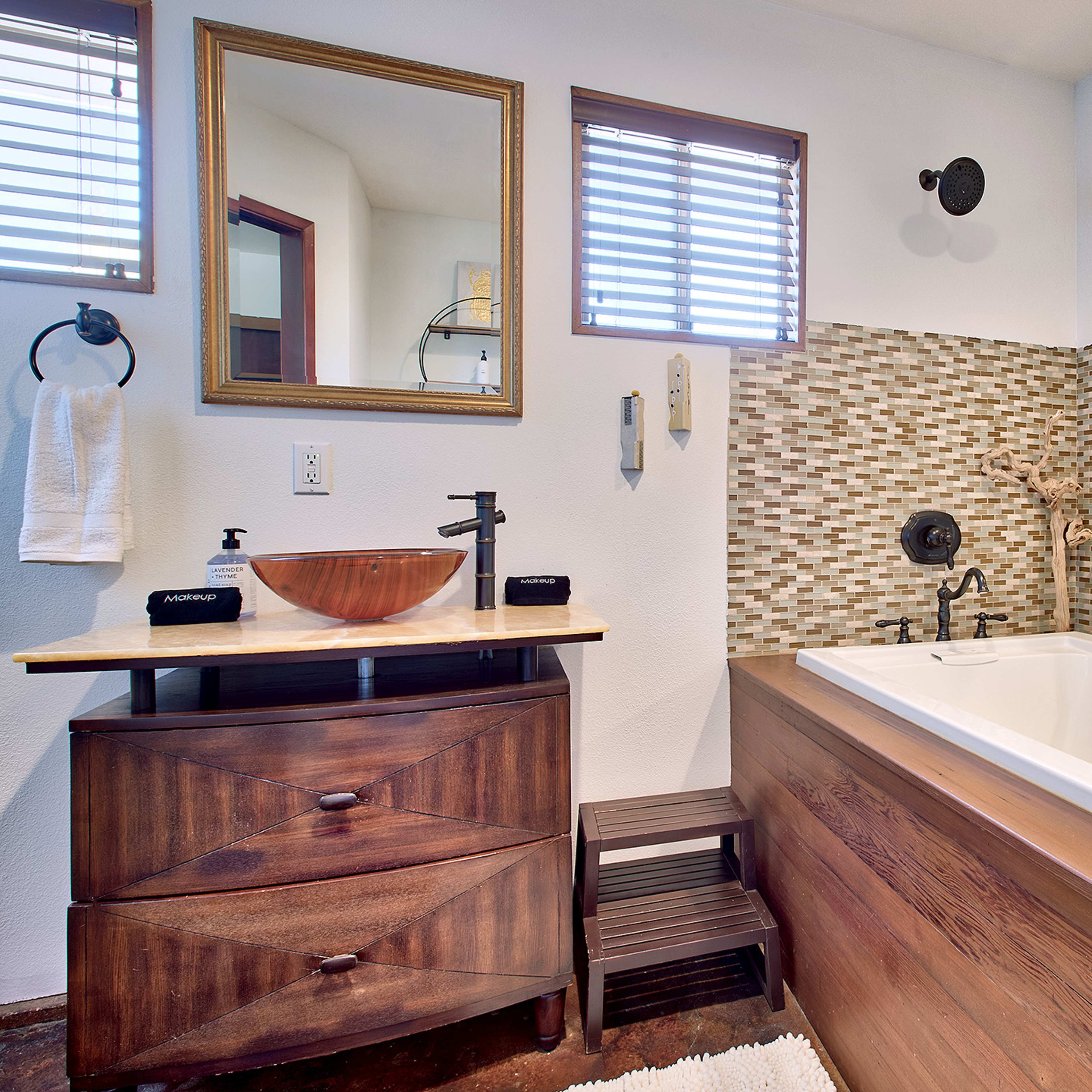 A modern bathroom featuring a freestanding bathtub, a wooden vanity with a bowl sink, and a mirrored wall.