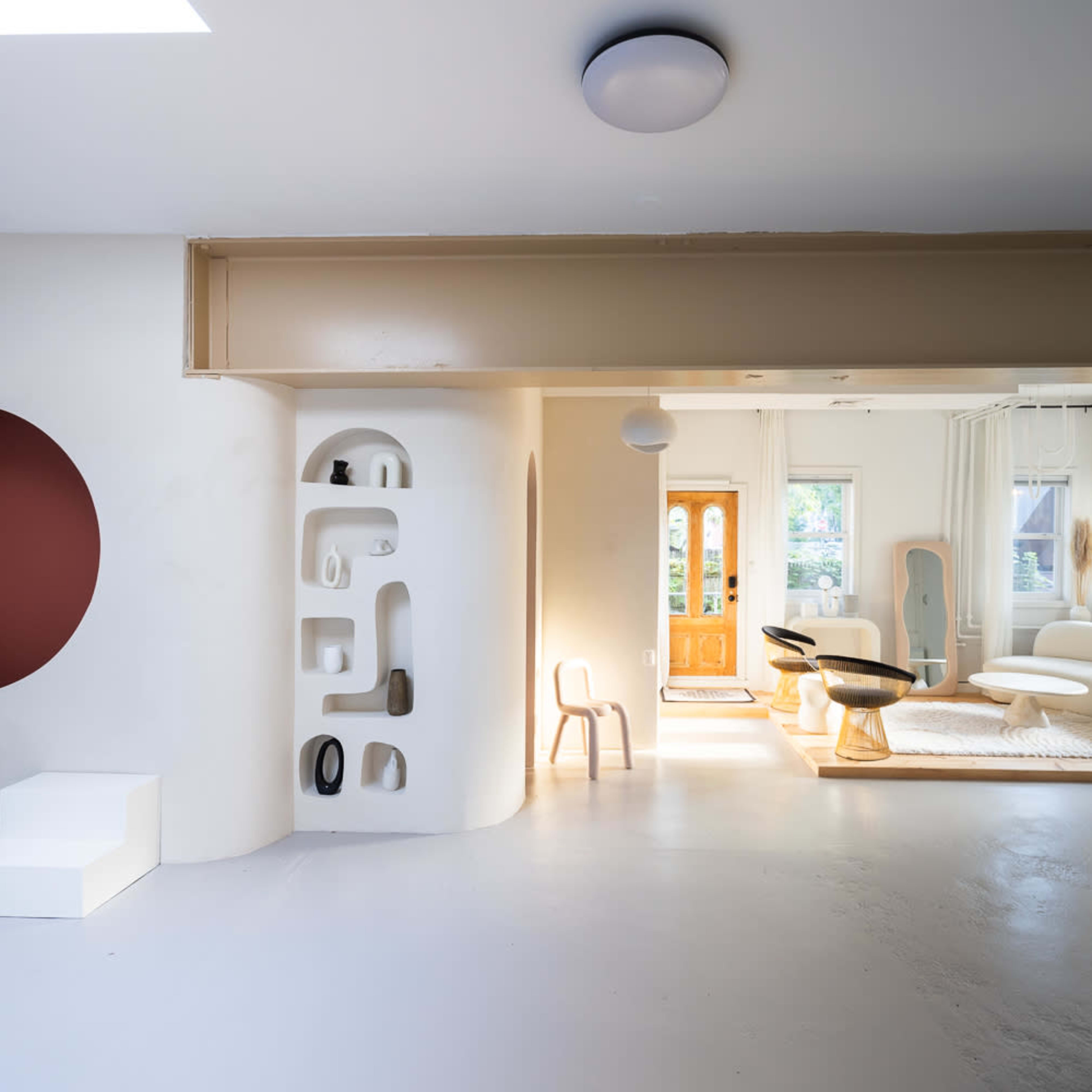 A spacious interior features a circular opening, sculptural wall shelves, a minimalist staircase, and modern furniture arranged around large windows.