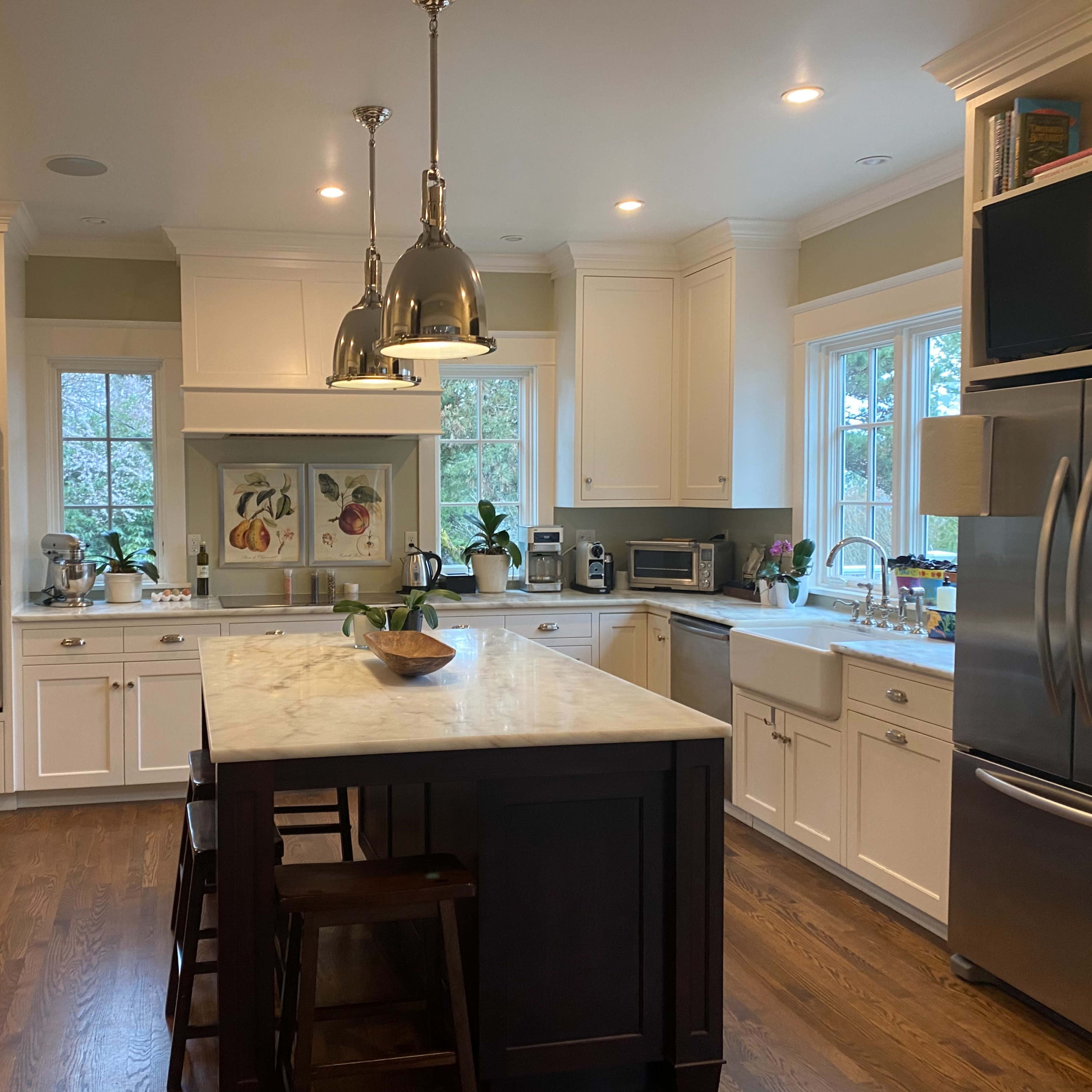 A brightly lit kitchen features white cabinetry, a central island with dark wood, and stainless steel appliances.