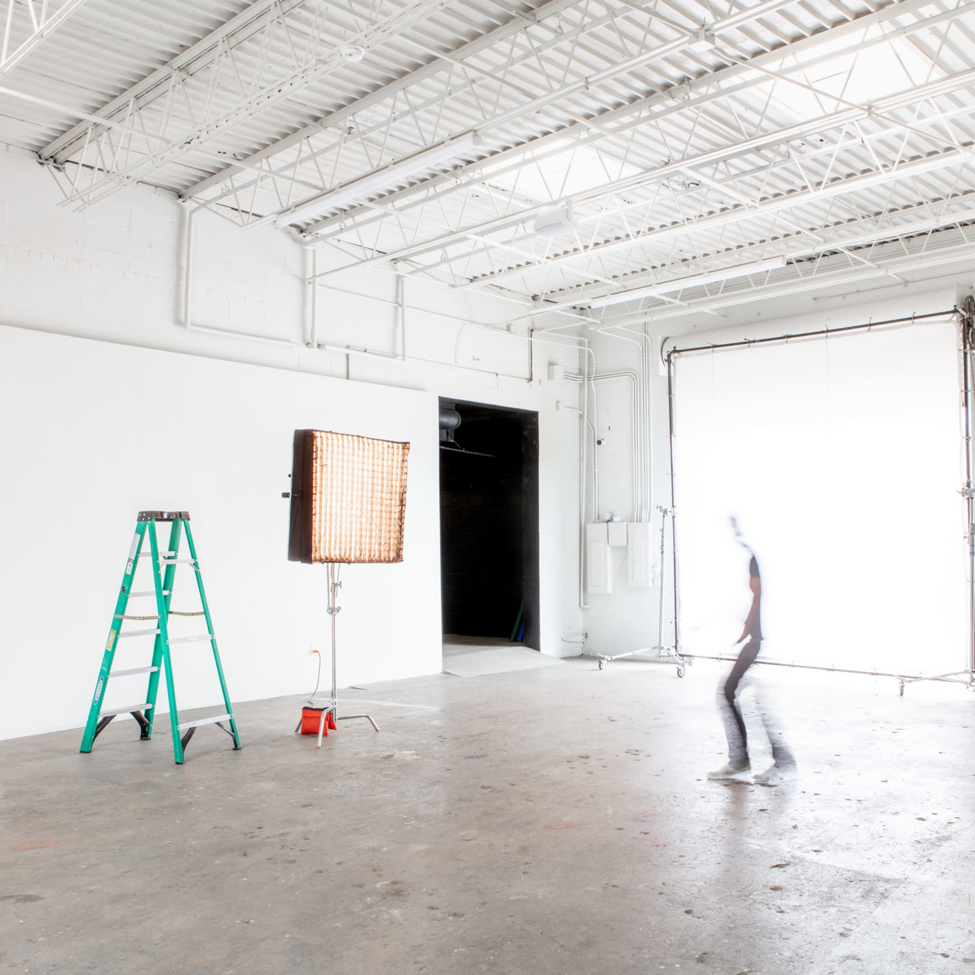 A person walks across an empty photo studio with a ladder and a light setup in the foreground.