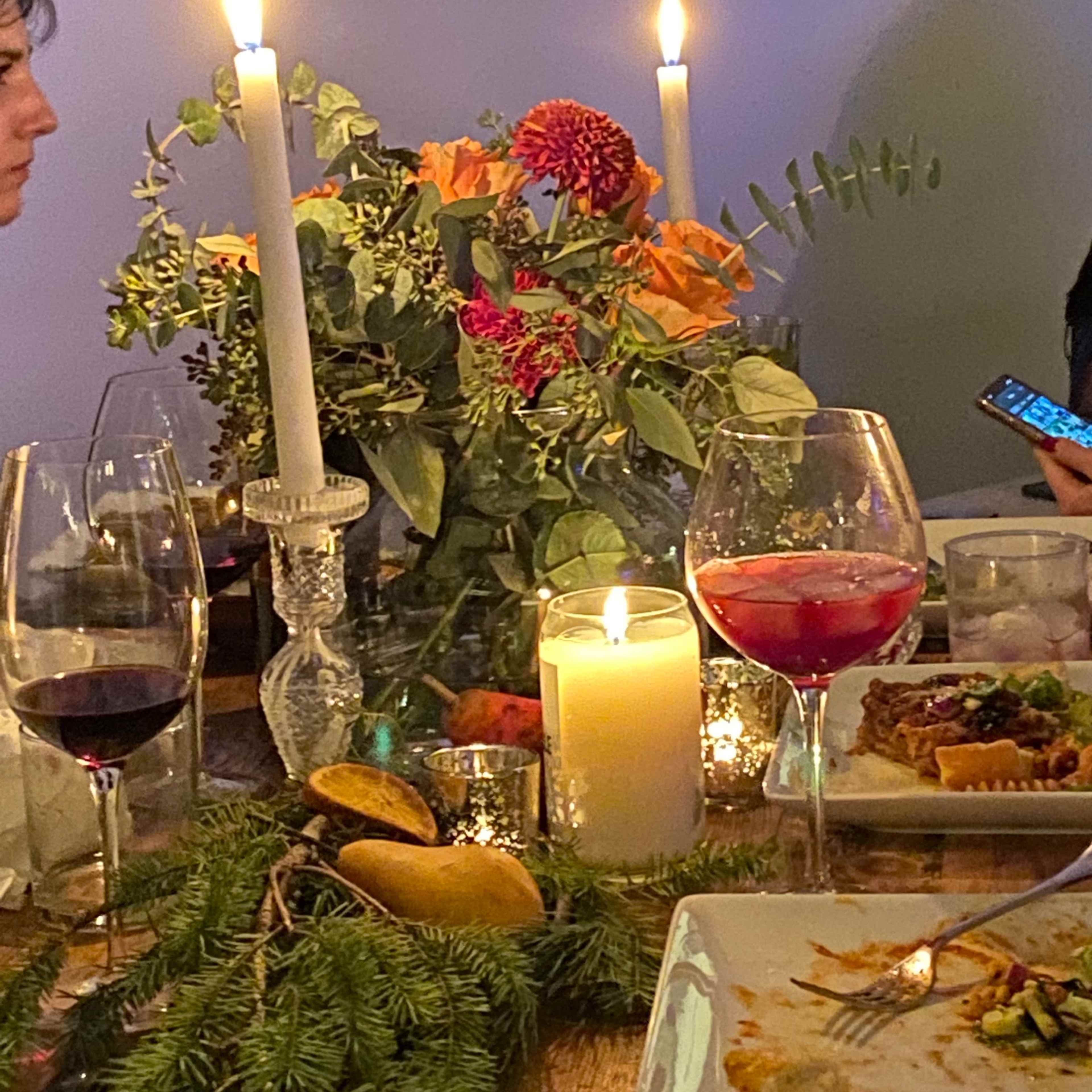 A candlelit dinner table is set with flowers, wine glasses, and plates of food, while two people engage in conversation.