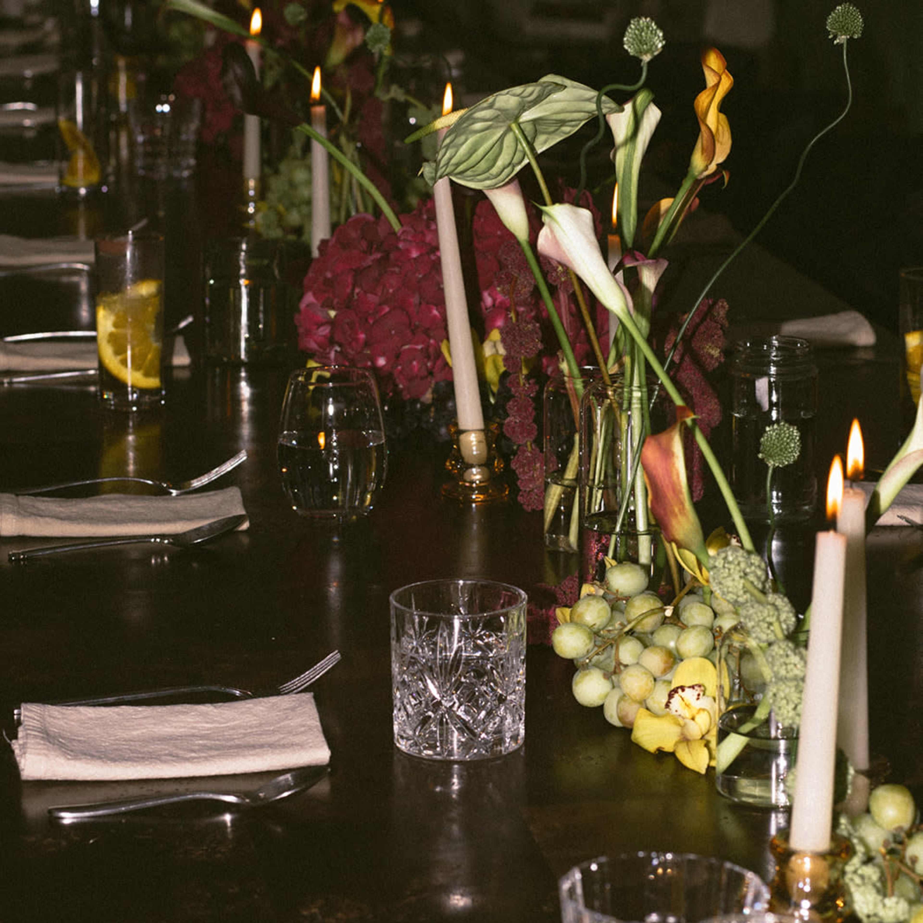 A long dining table is set with candles, glassware, and floral arrangements.