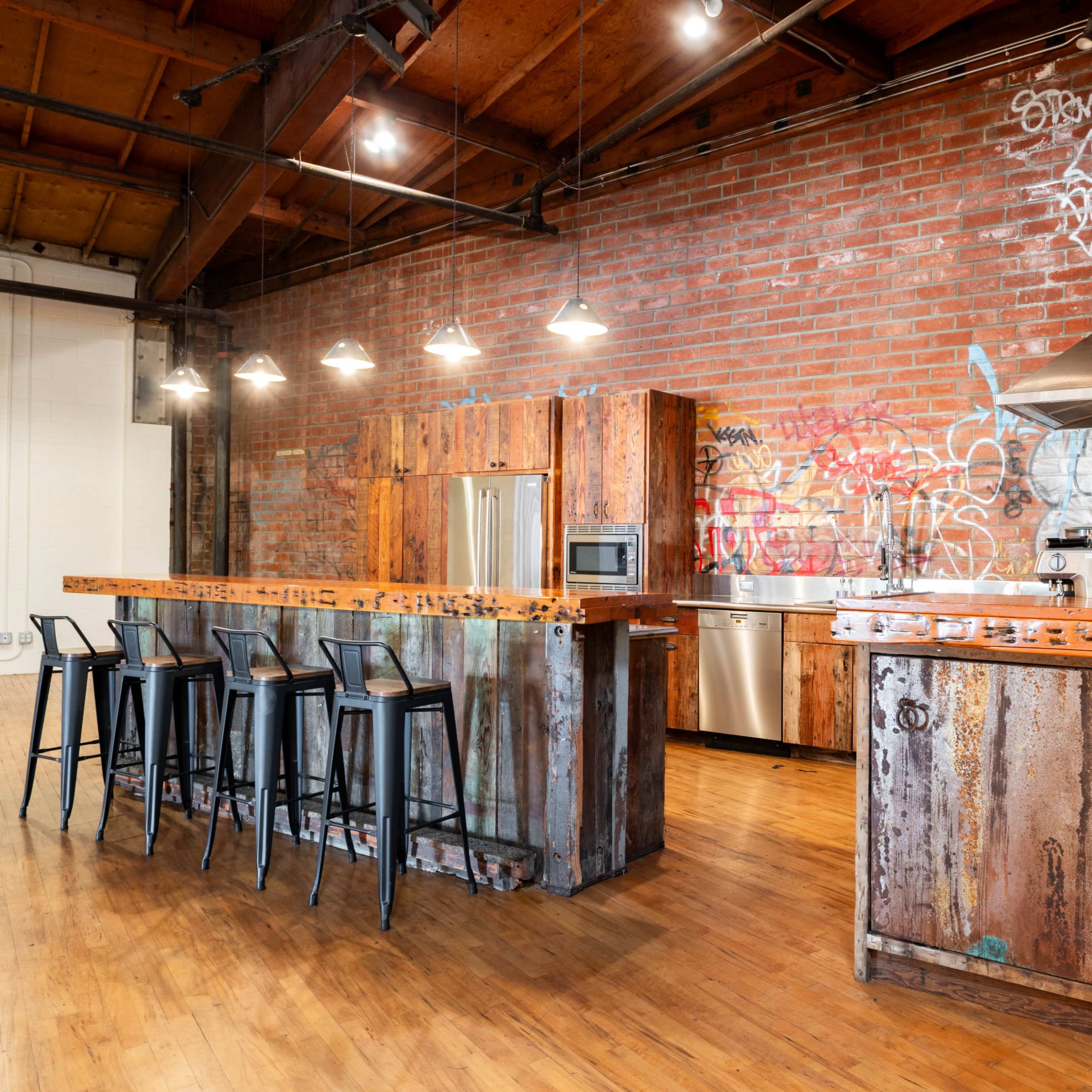 An industrial-style kitchen with a rustic wooden island and bar stools, featuring exposed brick walls and hanging pendant lights.
