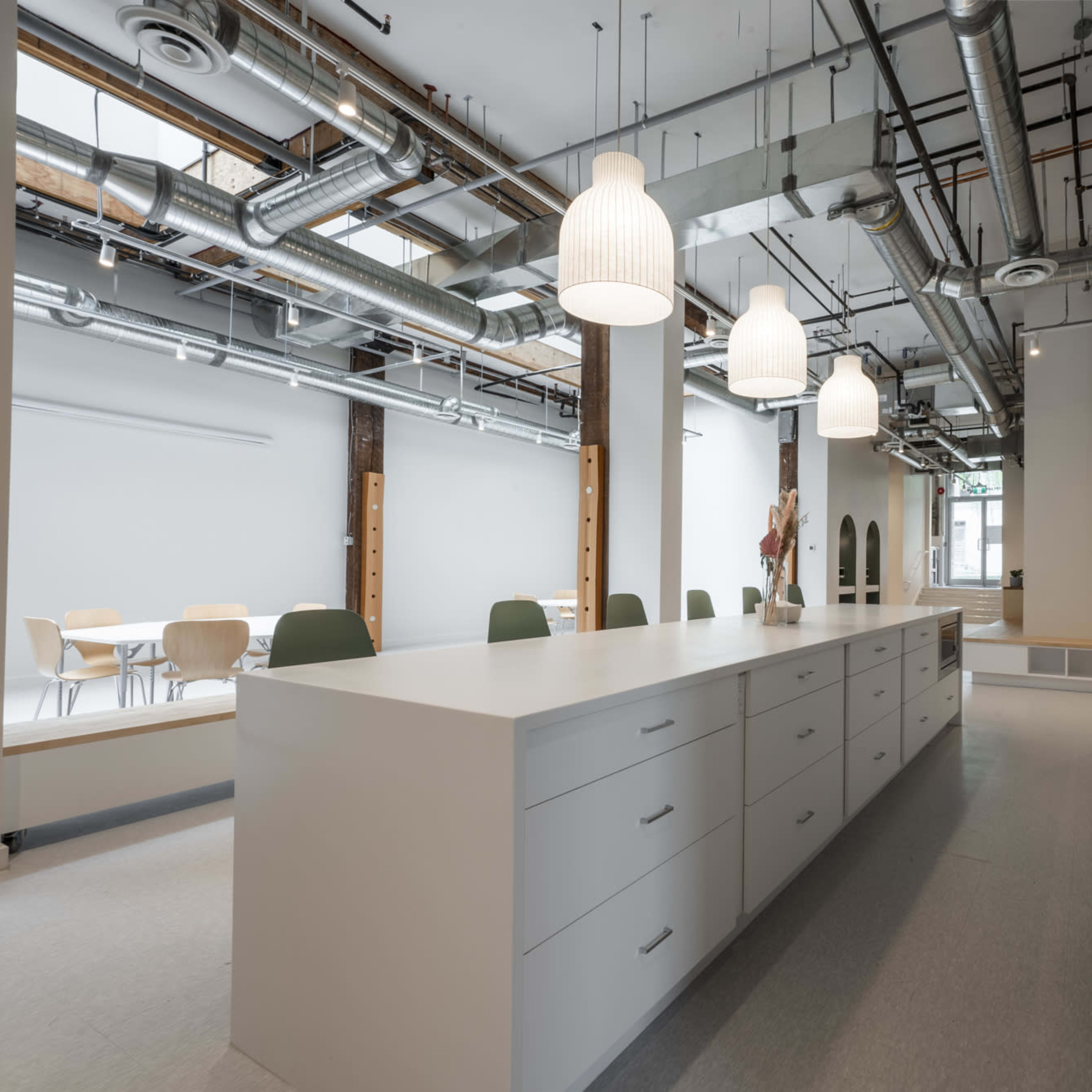 A modern kitchen with a large white island, overhead pendant lights, and exposed ductwork in an open space.