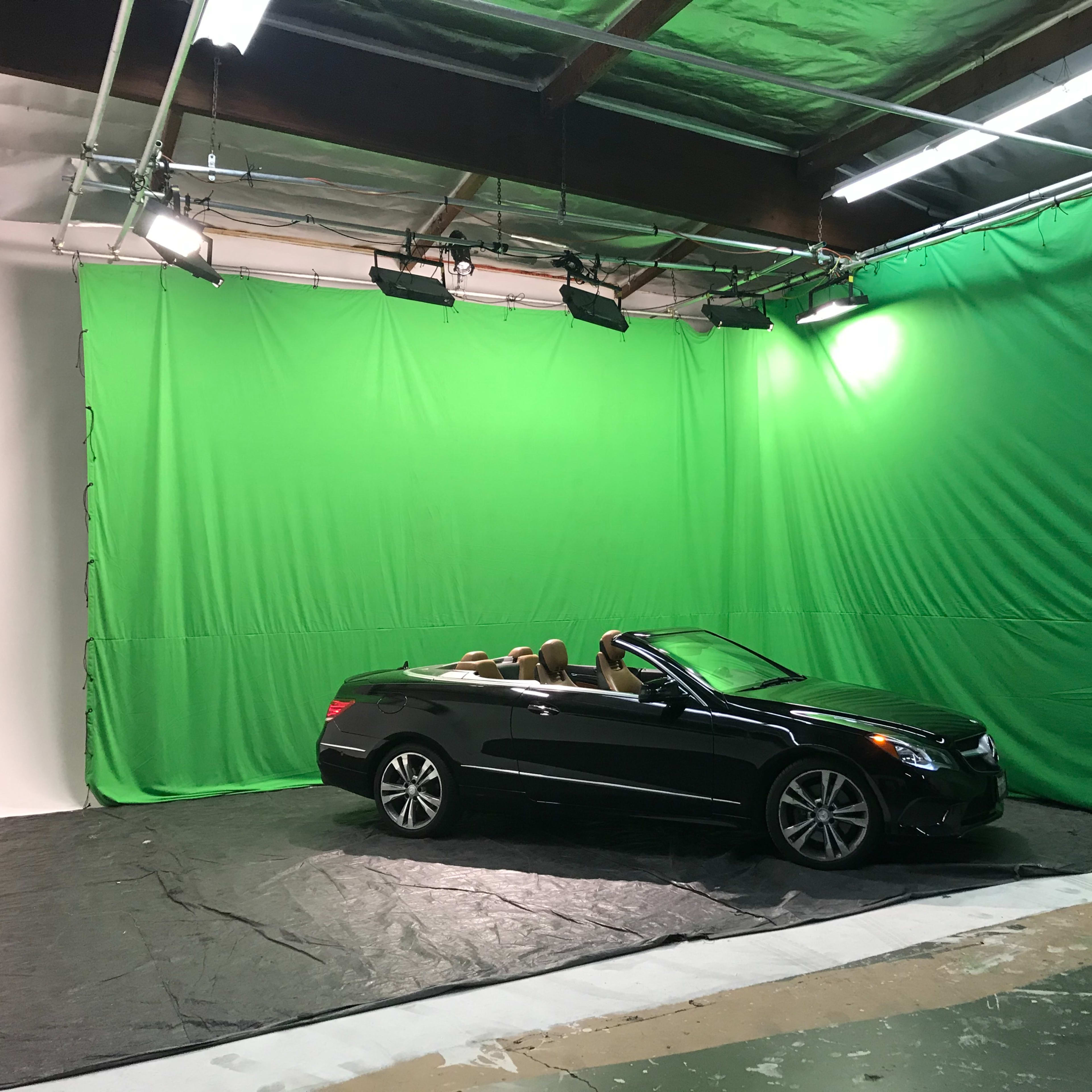 A black convertible car is positioned in front of a green screen in a studio space.