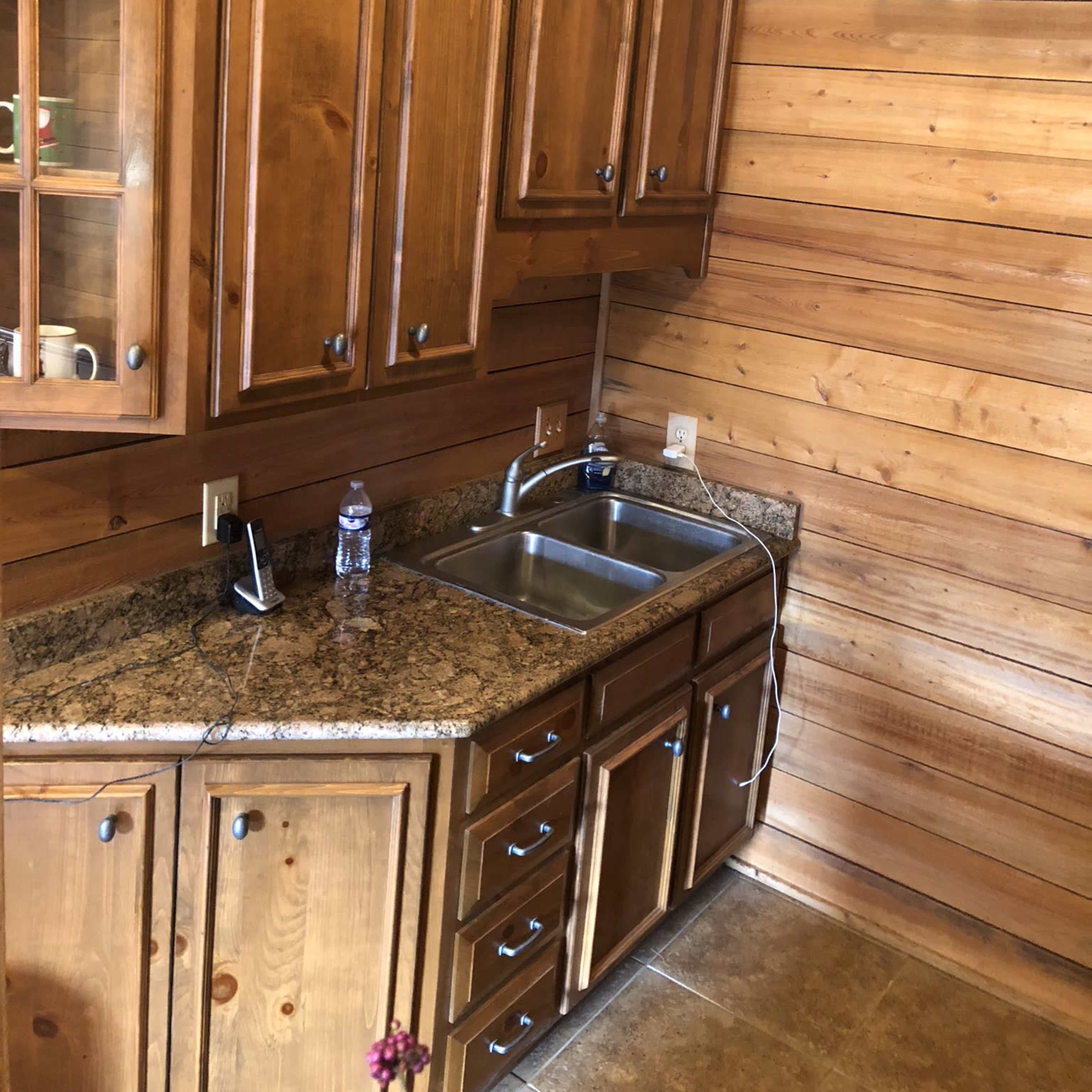 A wooden kitchen area with a stainless steel sink, granite countertops, and wooden cabinets.